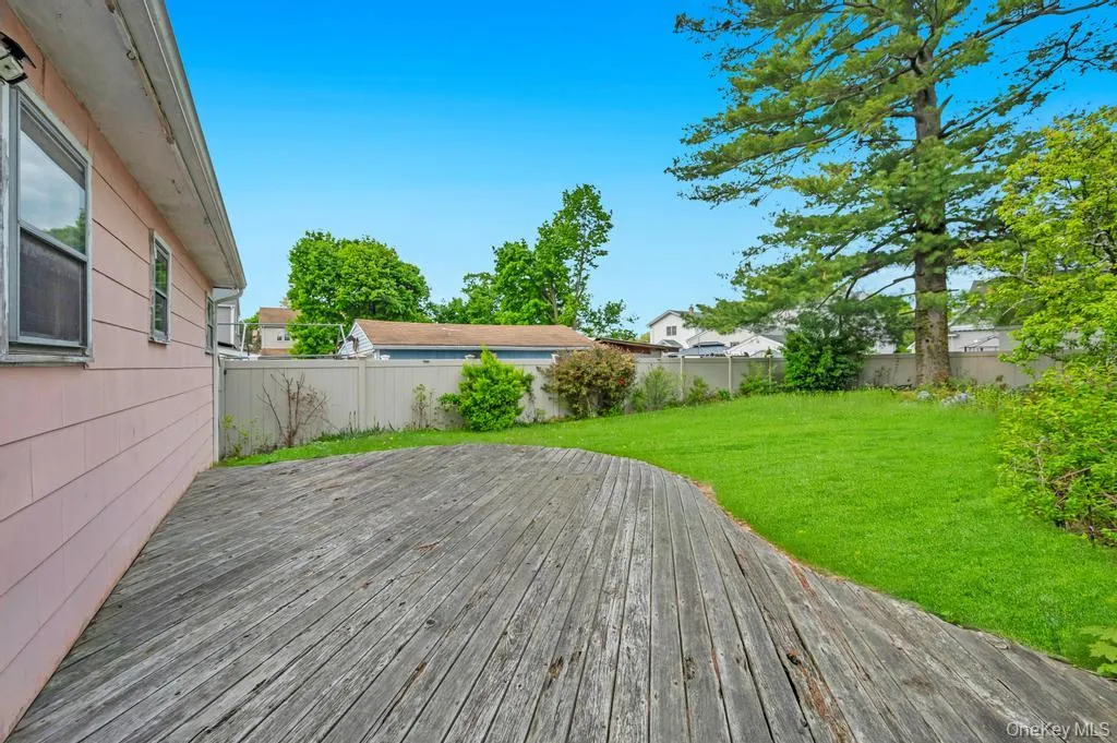 Expansive backyard featuring a curved wood deck, lush green lawn, mature trees, and a privacy fence Expansive backyard featuring a curved wood deck, lush green lawn, mature trees, and a privacy fence