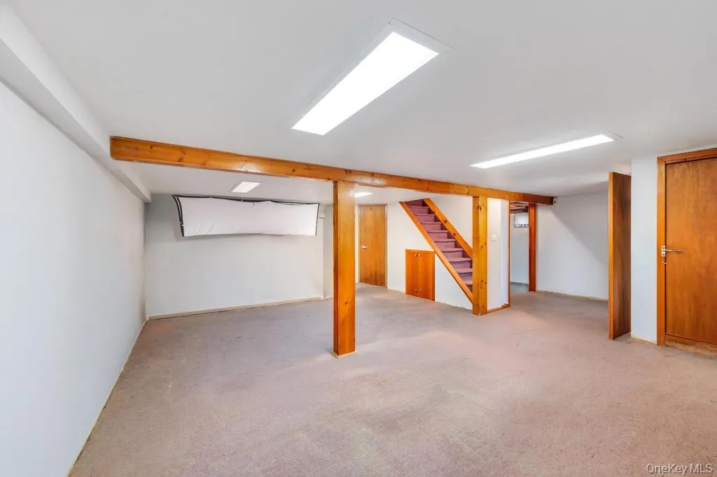 Finished basement space featuring wood support beams, recessed lighting, carpet flooring, and multiple wood-panel doors Finished basement space featuring wood support beams, recessed lighting, carpet flooring, and multiple wood-panel doors