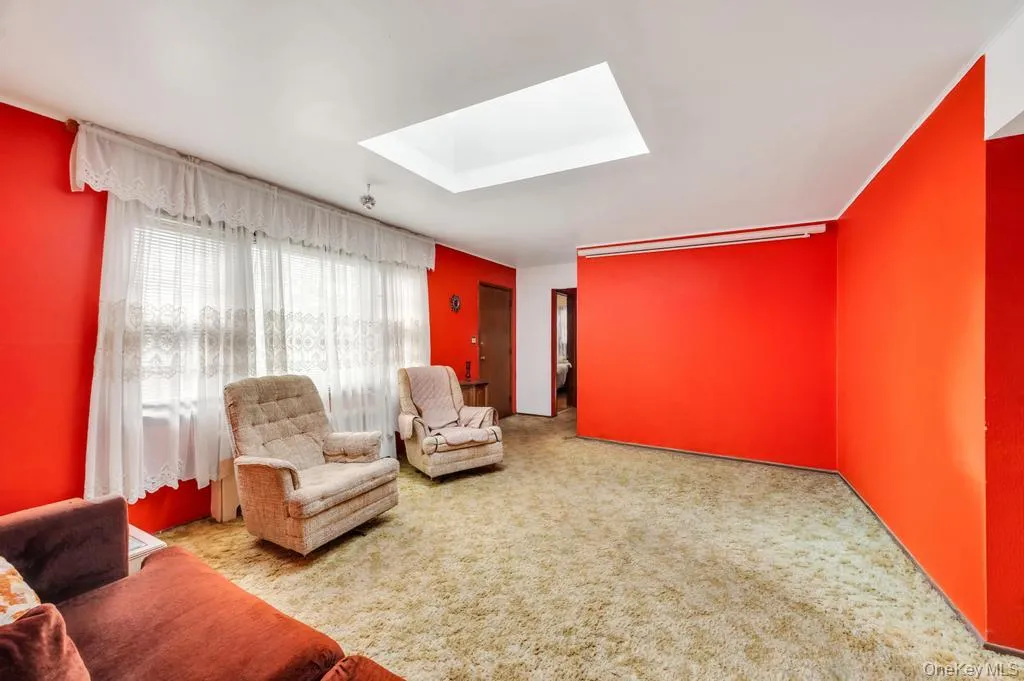 Living area featuring a skylight, window with blinds, and wall-to-wall carpeting Living area featuring a skylight, window with blinds, and wall-to-wall carpeting