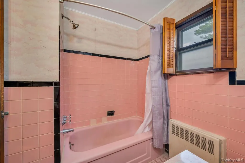 Bathroom featuring pink tiled walls with black accent trim, a built-in pink bathtub, and a shower with a chrome showerhead Bathroom featuring pink tiled walls with black accent trim, a built-in pink bathtub, and a shower with a chrome showerhead