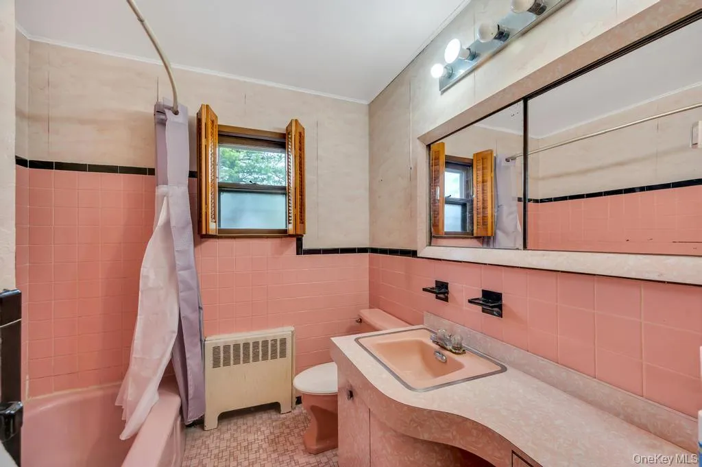 Bathroom featuring pink wall tiling with black accent trim, a built-in vanity with integrated sink, and an expansive mirrored cabinet above Bathroom featuring pink wall tiling with black accent trim, a built-in vanity with integrated sink, and an expansive mirrored cabinet above