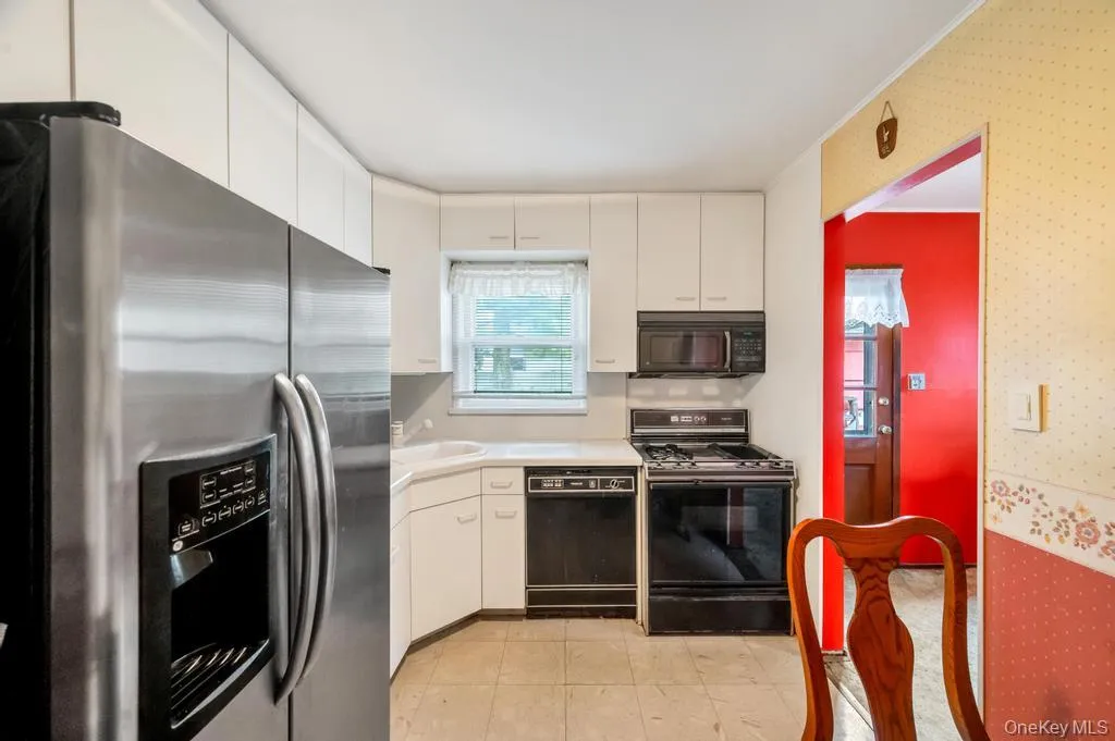 Kitchen featuring white cabinetry, white countertops, stainless steel refrigerator, black gas range, and black dishwasher Kitchen featuring white cabinetry, white countertops, stainless steel refrigerator, black gas range, and black dishwasher