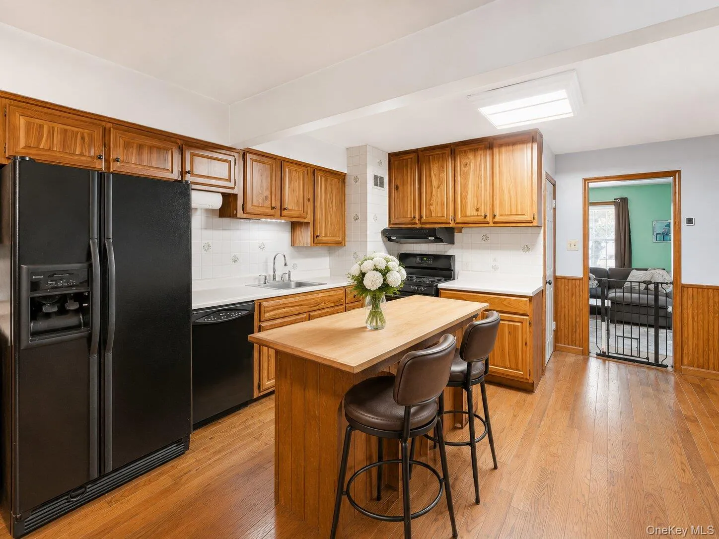 Spacious kitchen featuring abundant wood cabinetry, black appliances, hardwood floors, a center island, and seating for two. Spacious kitchen featuring abundant wood cabinetry, black appliances, hardwood floors, a center island, and seating for two.