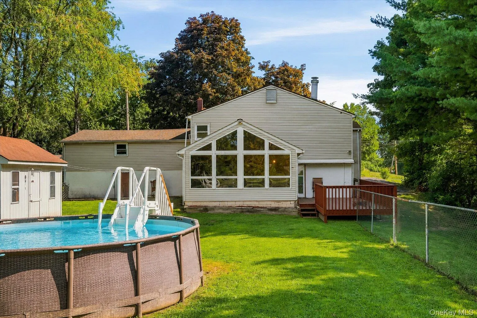 Spacious fenced backyard with an above-ground pool, storage shed, deck, and enclosed rear addition overlooking the property. Spacious fenced backyard with an above-ground pool, storage shed, deck, and enclosed rear addition overlooking the property.