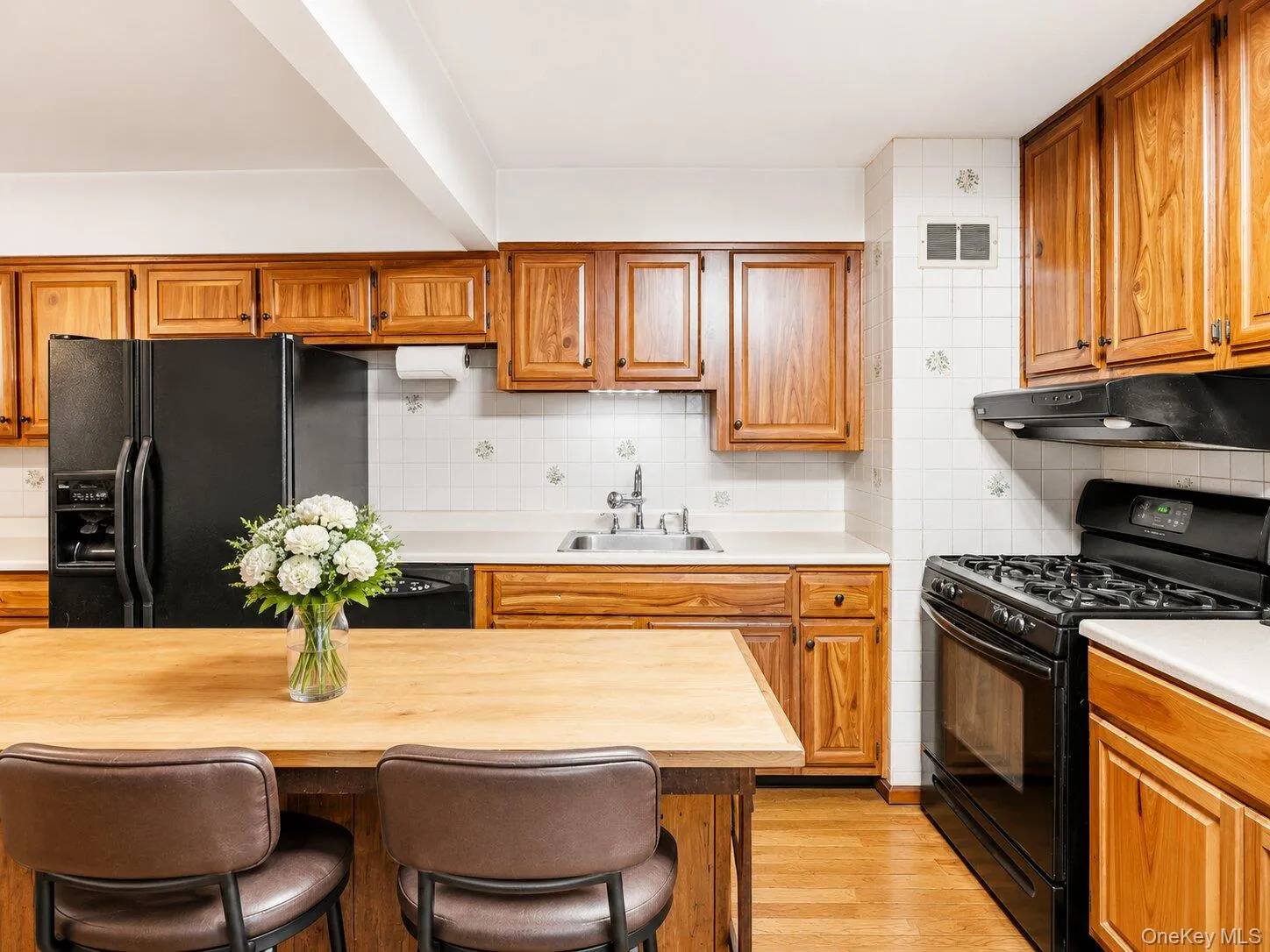Spacious kitchen featuring abundant wood cabinetry, black appliances, hardwood floors, a center island, and seating for two. Spacious kitchen featuring abundant wood cabinetry, black appliances, hardwood floors, a center island, and seating for two.