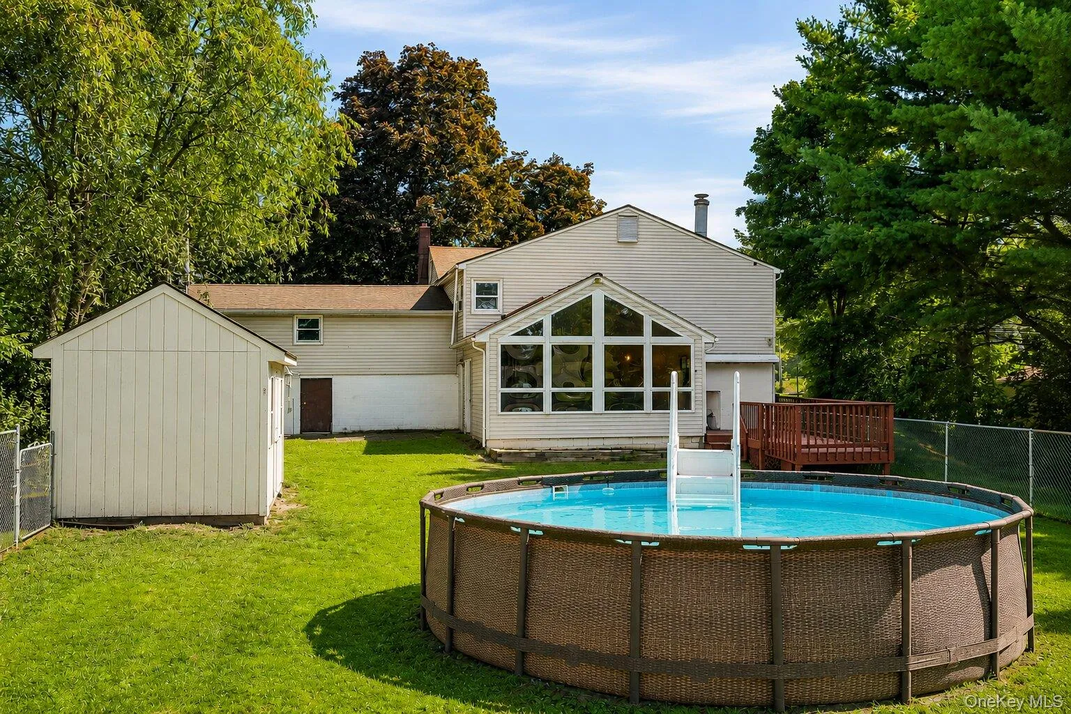 Spacious fenced backyard with an above-ground pool, storage shed, deck, and enclosed rear addition overlooking the property. Spacious fenced backyard with an above-ground pool, storage shed, deck, and enclosed rear addition overlooking the property.