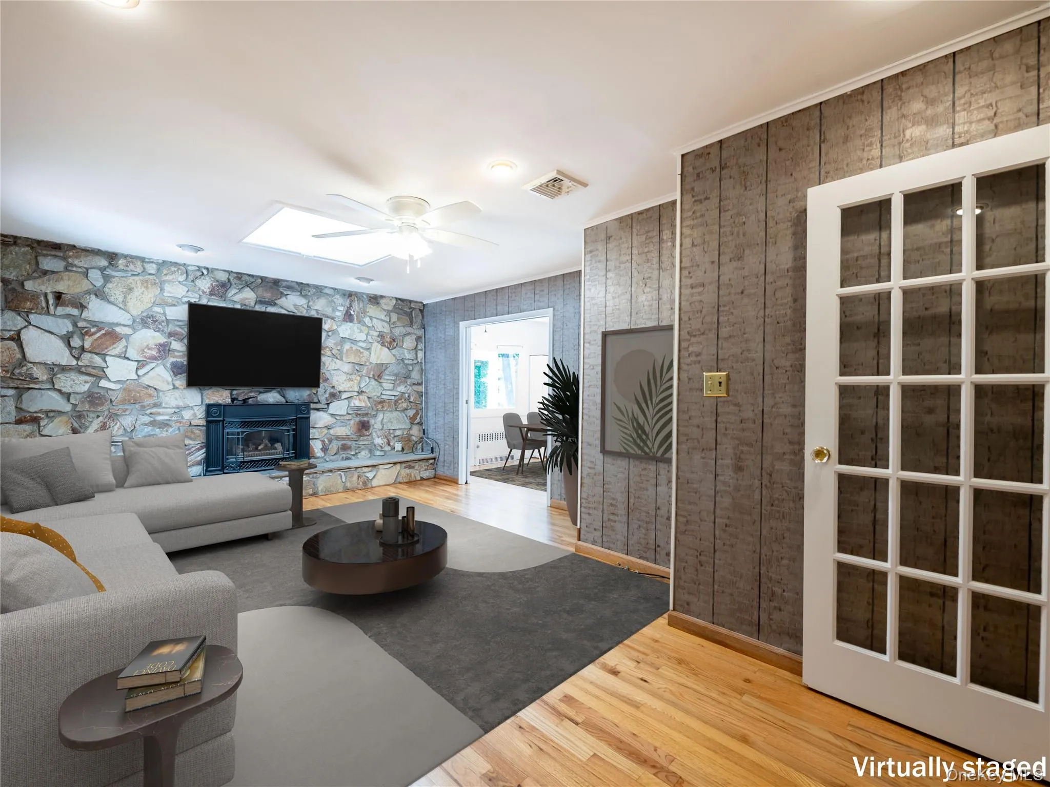 Living area with wood finished floors, a ceiling fan, a stone fireplace, and a skylight Living area with wood finished floors, a ceiling fan, a stone fireplace, and a skylight
