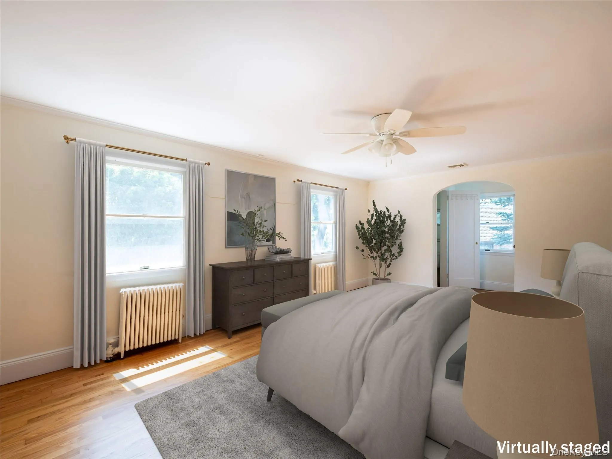 Bedroom featuring radiator heating unit, multiple windows, arched walkways, and light wood-type flooring Bedroom featuring radiator heating unit, multiple windows, arched walkways, and light wood-type flooring