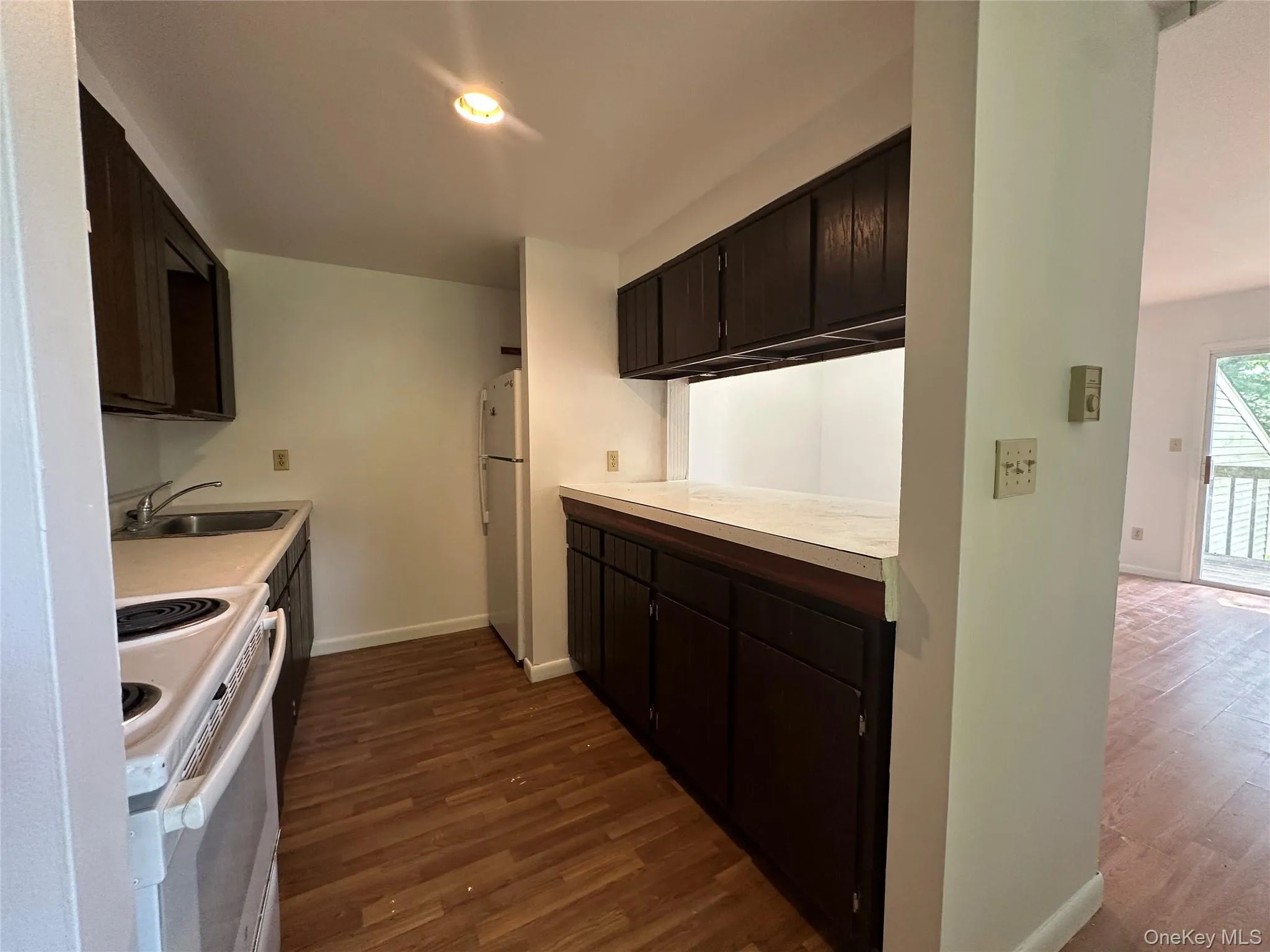 Kitchen with white appliances, dark wood-type flooring, a sink, baseboards, and light countertops Kitchen with white appliances, dark wood-type flooring, a sink, baseboards, and light countertops