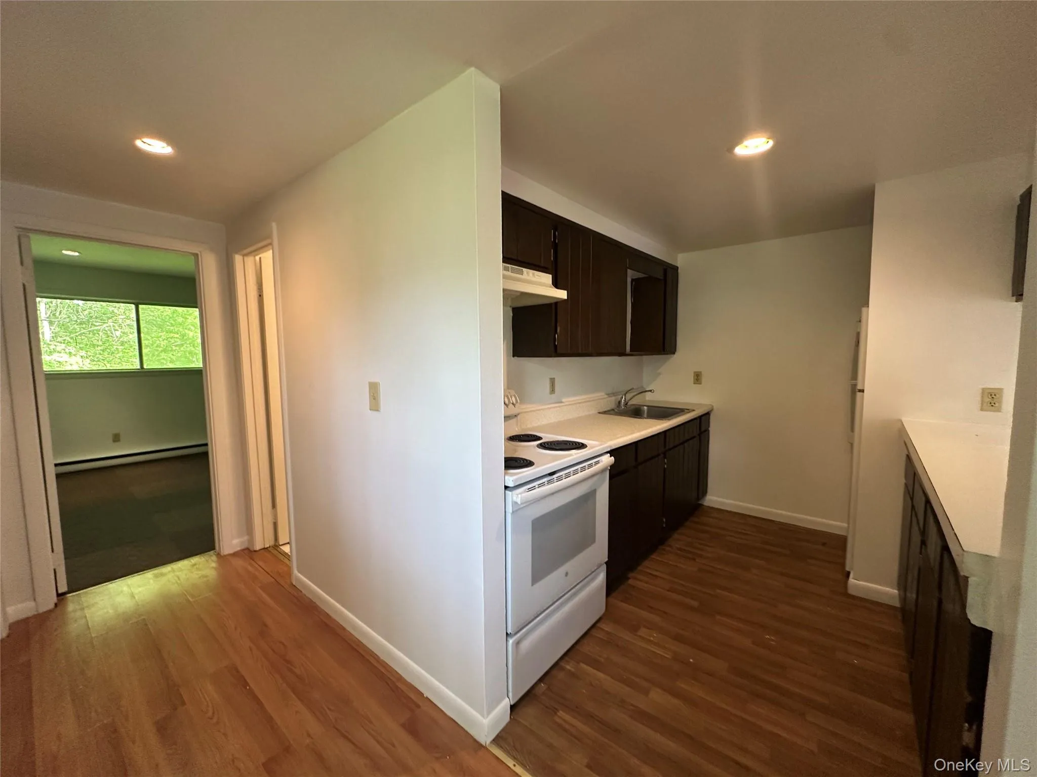 Kitchen with white appliances, under cabinet range hood, a sink, a baseboard radiator, and dark wood-type flooring Kitchen with white appliances, under cabinet range hood, a sink, a baseboard radiator, and dark wood-type flooring