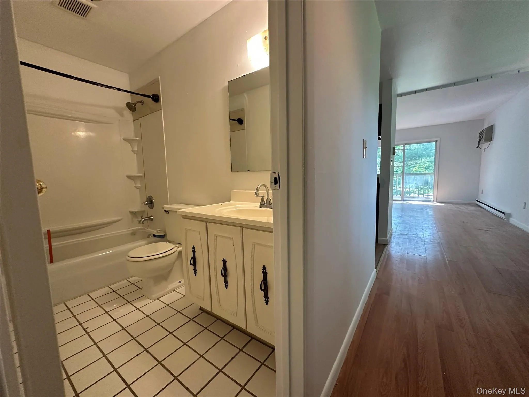 Bathroom with vanity, baseboard heating, shower / bathtub combination, toilet, and wood finished floors Bathroom with vanity, baseboard heating, shower / bathtub combination, toilet, and wood finished floors