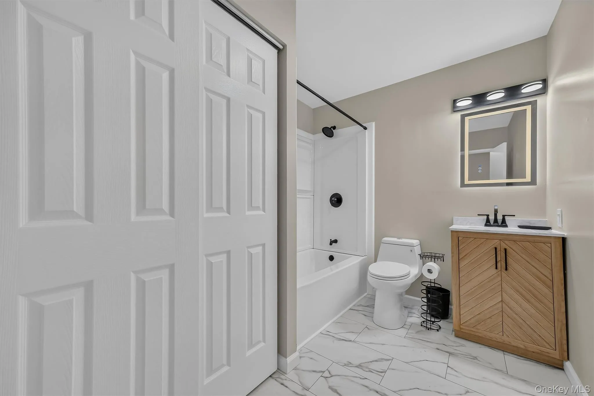 Updated Full Bathroom – Bright, refreshed bathroom featuring marble-look tile flooring, a modern wood vanity, illuminated mirror, matte-black fixtures, and a tub-and-shower combination. Updated Full Bathroom – Bright, refreshed bathroom featuring marble-look tile flooring, a modern wood vanity, illuminated mirror, matte-black fixtures, and a tub-and-shower combination.
