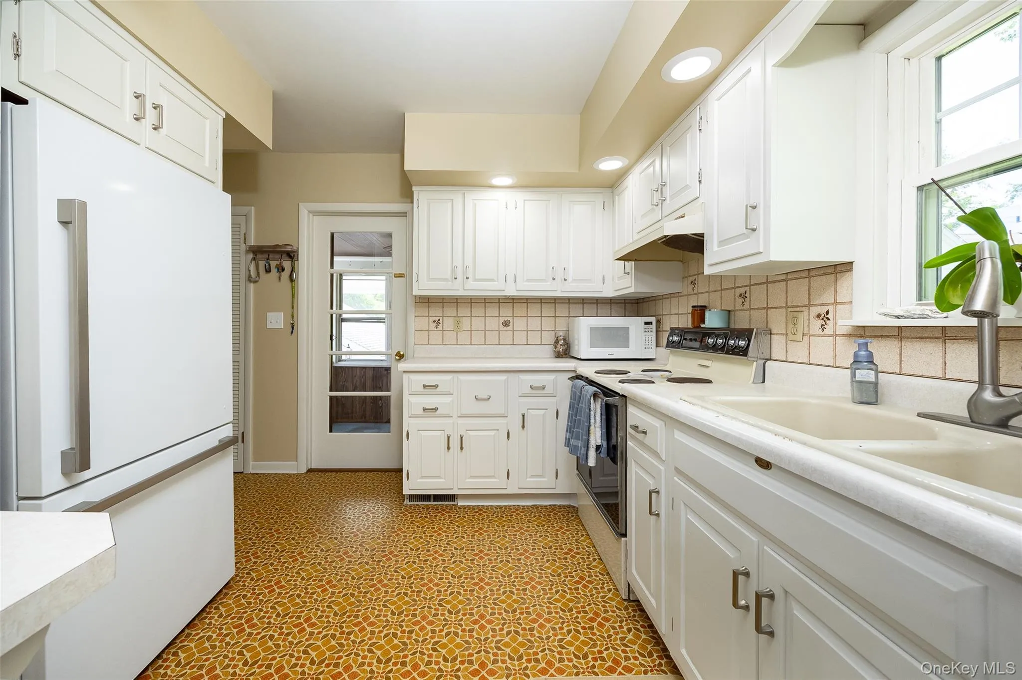 Kitchen featuring white cabinetry, light-toned countertops, patterned flooring, a window, and recessed lighting Kitchen featuring white cabinetry, light-toned countertops, patterned flooring, a window, and recessed lighting
