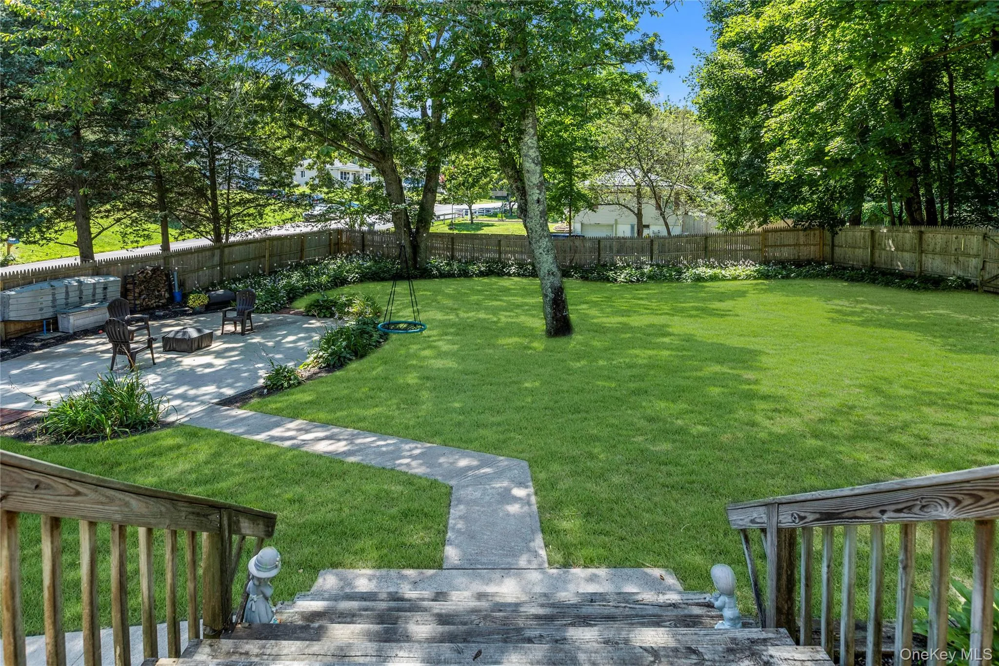 Expansive backyard featuring a lush lawn, mature trees, and a concrete patio with a fire pit area Expansive backyard featuring a lush lawn, mature trees, and a concrete patio with a fire pit area