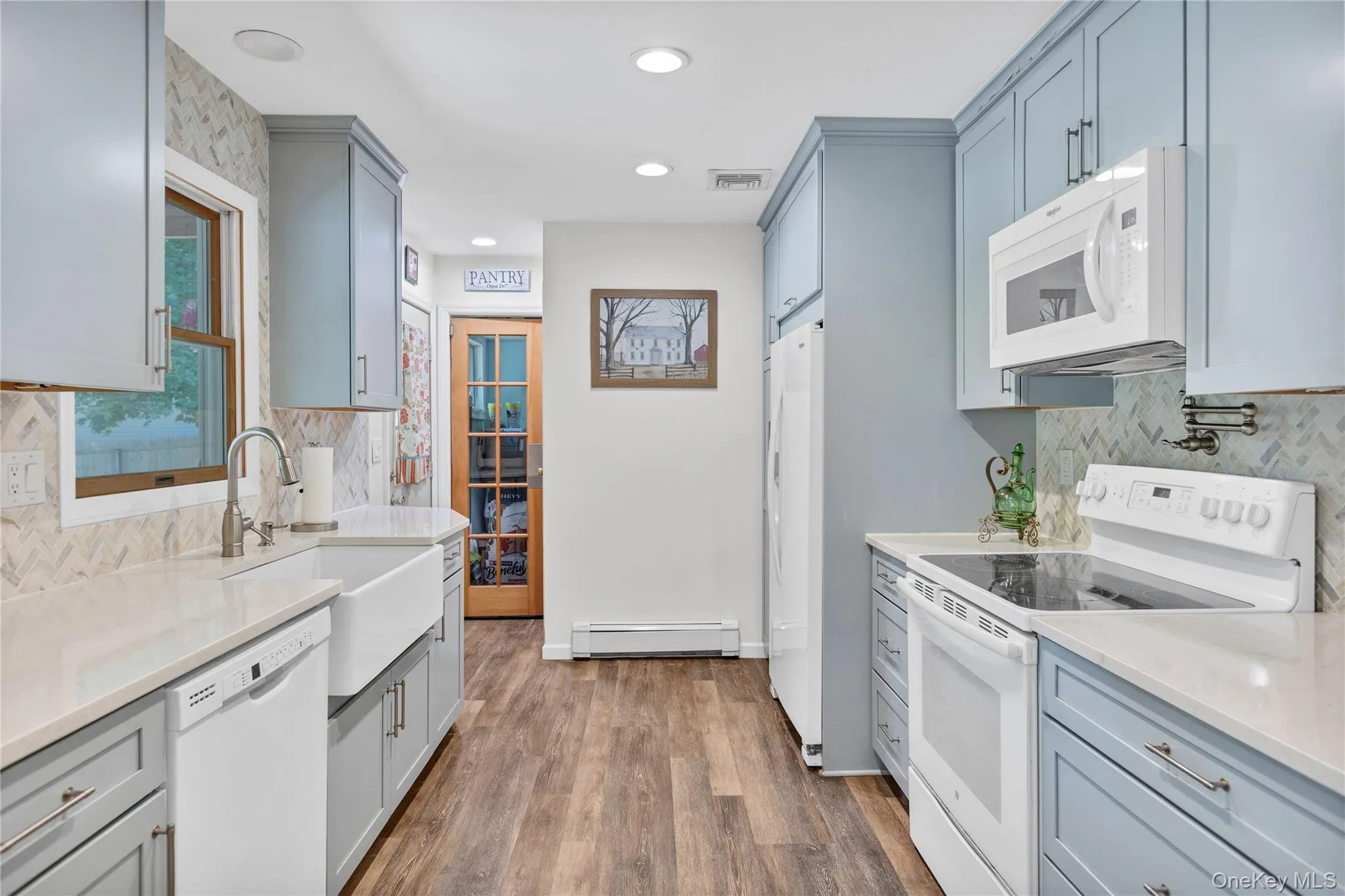 Kitchen featuring light blue cabinetry, white countertops, wood-finish flooring, a white farmhouse sink, and a herringbone pattern tile backsplash Kitchen featuring light blue cabinetry, white countertops, wood-finish flooring, a white farmhouse sink, and a herringbone pattern tile backsplash