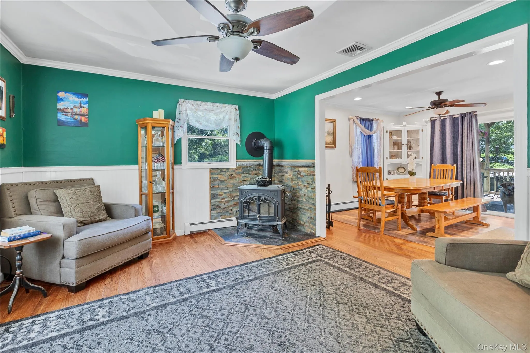 Living area featuring wood-finish flooring, a wood-burning stove with a stacked stone surround, and crown molding Living area featuring wood-finish flooring, a wood-burning stove with a stacked stone surround, and crown molding