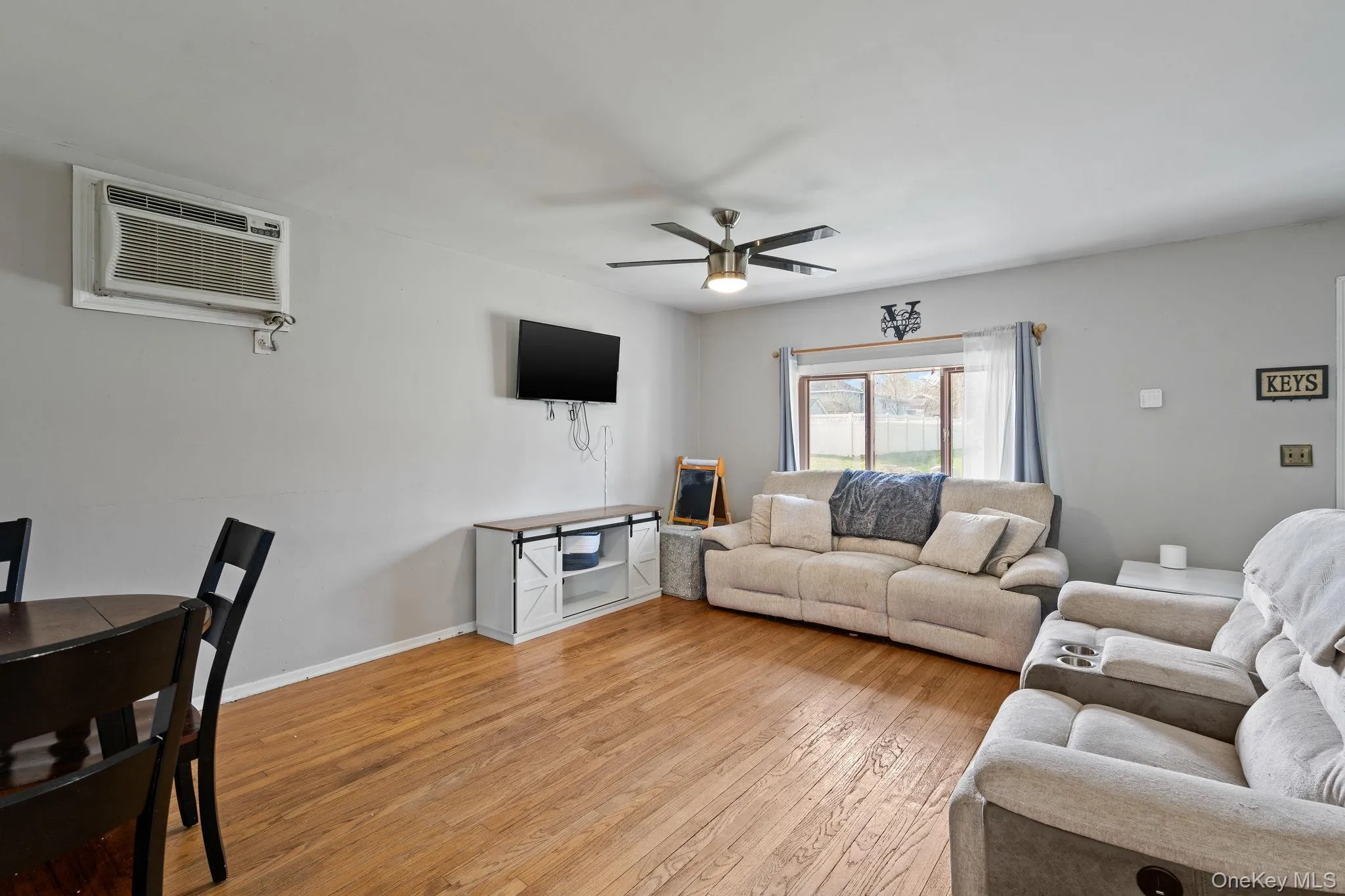 Living area with a ceiling fan, light wood-style flooring, a wall mounted AC, and baseboards Living area with a ceiling fan, light wood-style flooring, a wall mounted AC, and baseboards