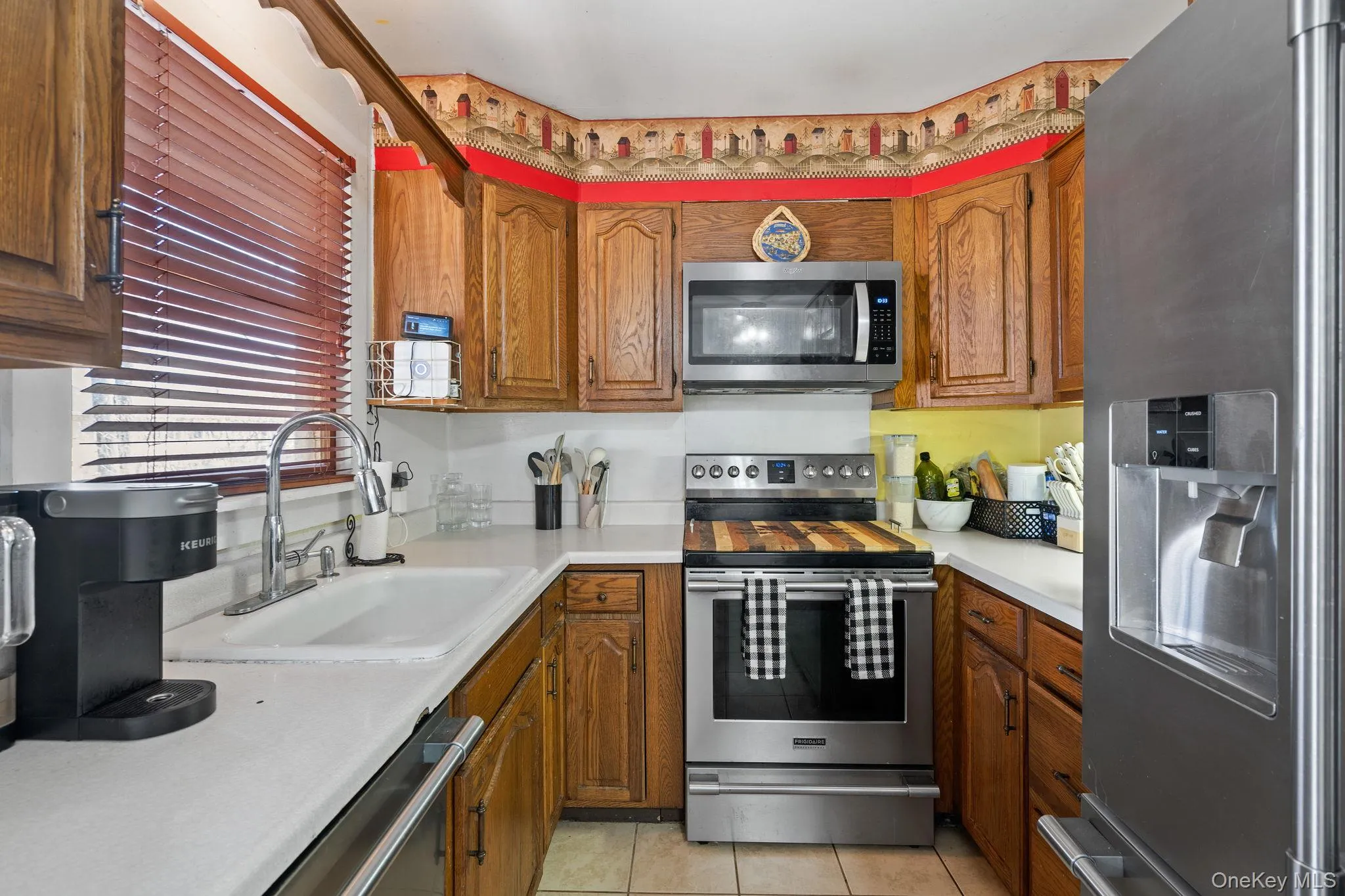 Kitchen featuring a sink, brown cabinetry, light tile patterned floors, and appliances with stainless steel finishes Kitchen featuring a sink, brown cabinetry, light tile patterned floors, and appliances with stainless steel finishes
