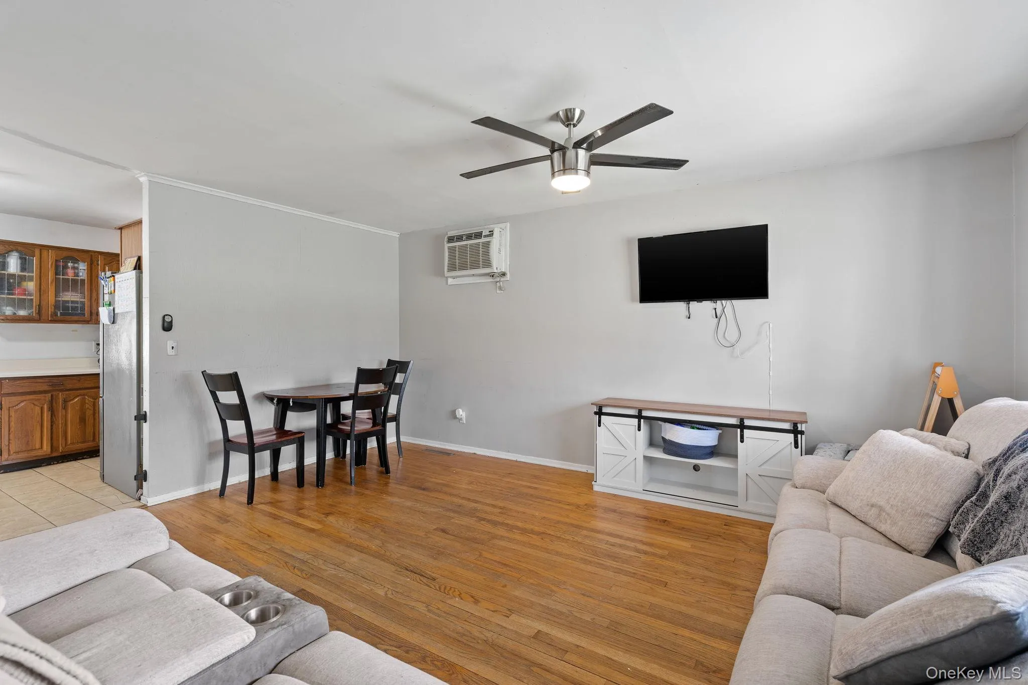 Living room with baseboards, a wall mounted AC, light wood-style flooring, and ceiling fan Living room with baseboards, a wall mounted AC, light wood-style flooring, and ceiling fan