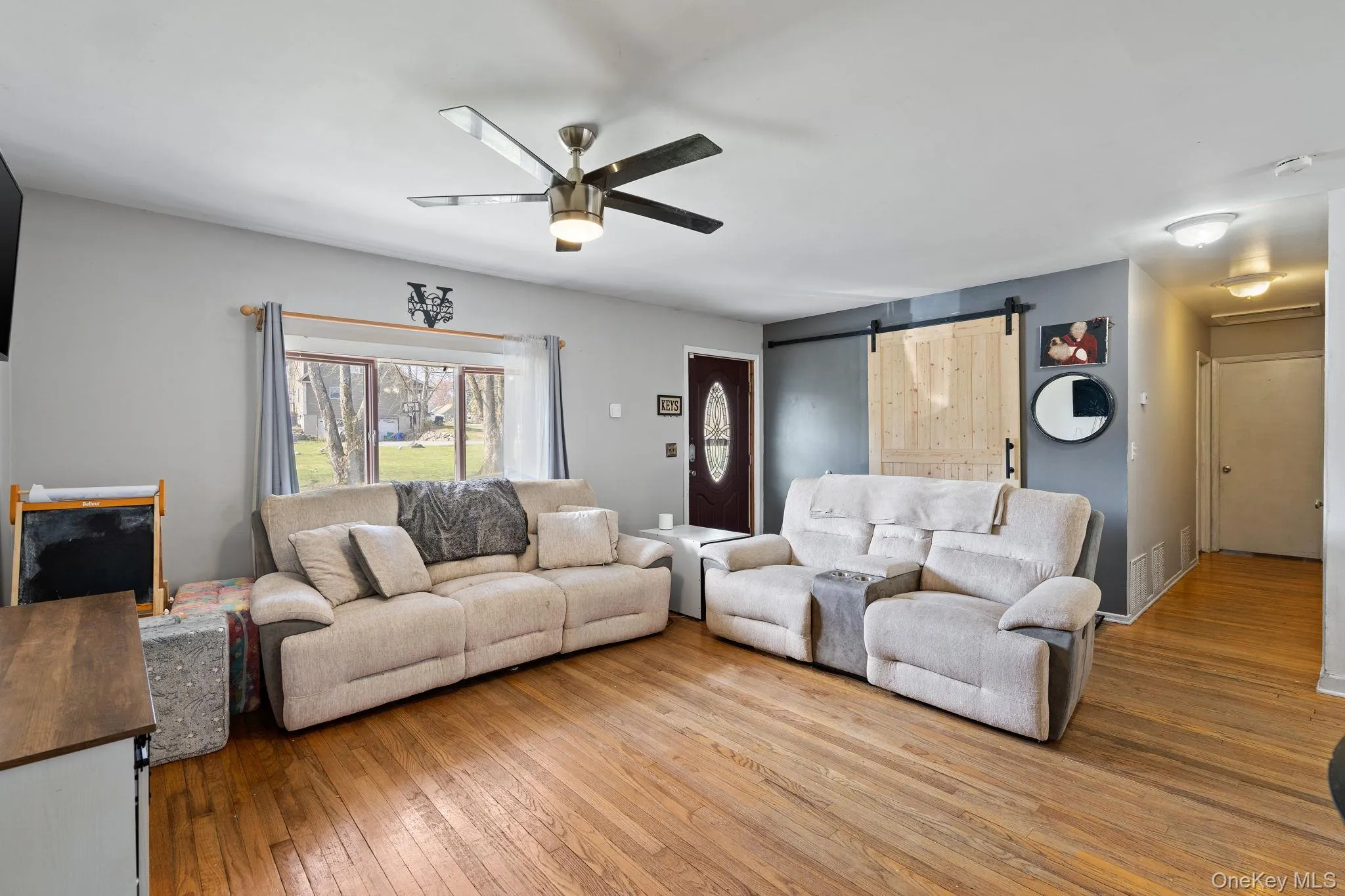Living room with a barn door, ceiling fan, visible vents, and hardwood / wood-style flooring Living room with a barn door, ceiling fan, visible vents, and hardwood / wood-style flooring