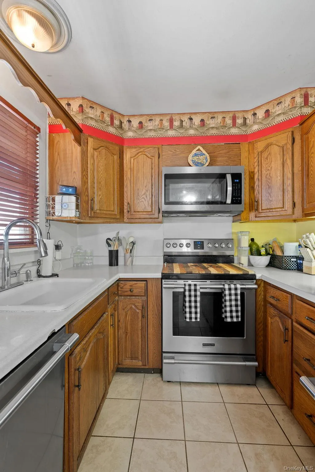 Kitchen featuring light countertops, appliances with stainless steel finishes, a sink, brown cabinetry, and light tile patterned floors Kitchen featuring light countertops, appliances with stainless steel finishes, a sink, brown cabinetry, and light tile patterned floors