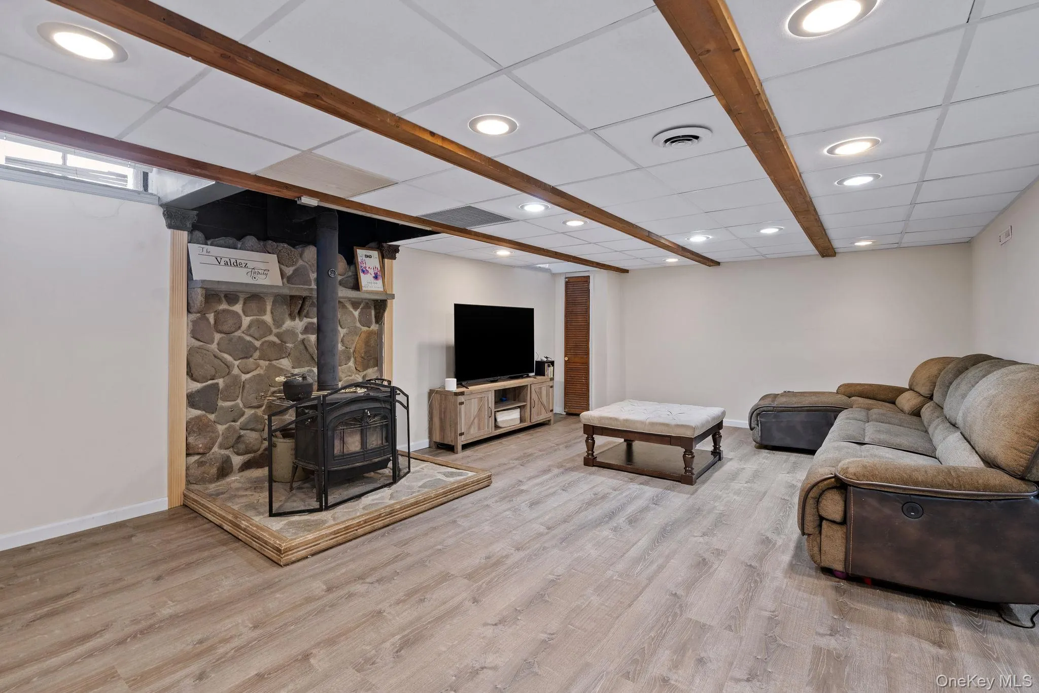 Living room featuring visible vents, wood finished floors, a wood stove, and a paneled ceiling Living room featuring visible vents, wood finished floors, a wood stove, and a paneled ceiling