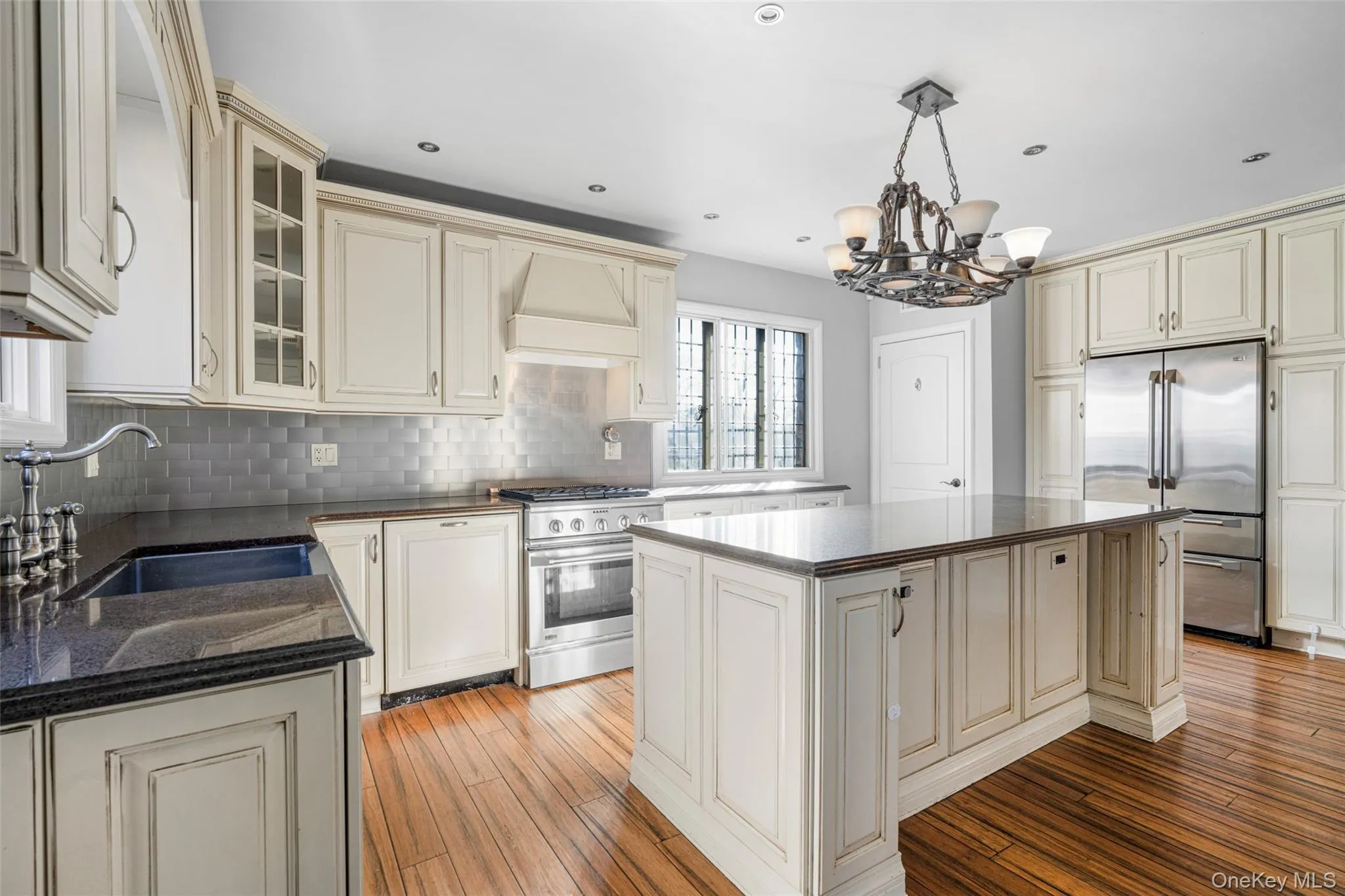 Kitchen with cream cabinetry, a center island, custom range hood, high end appliances, and sink Kitchen with cream cabinetry, a center island, custom range hood, high end appliances, and sink