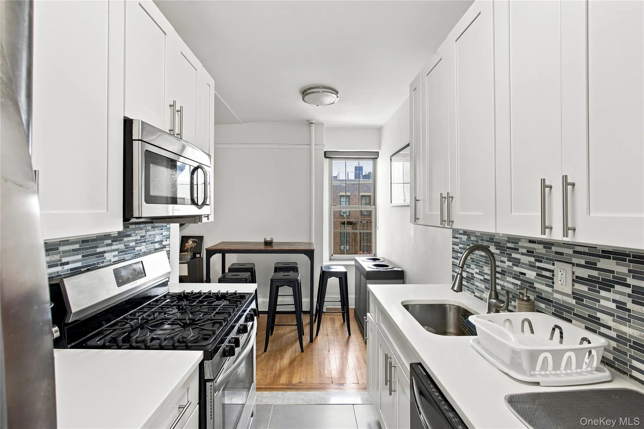 Galley kitchen featuring white shaker cabinetry, stainless steel appliances, mosaic tile backsplash, and light-toned countertops Galley kitchen featuring white shaker cabinetry, stainless steel appliances, mosaic tile backsplash, and light-toned countertops