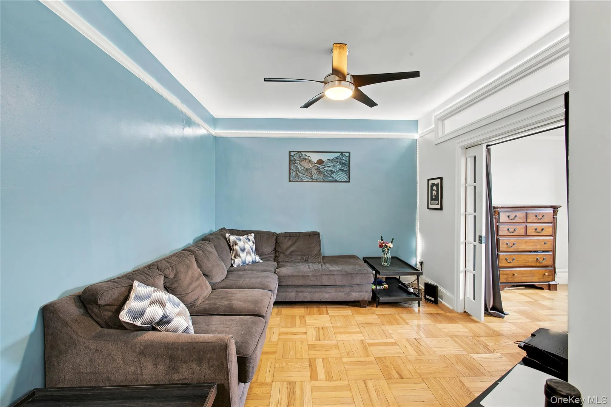 Living area featuring parquet wood flooring, crown molding, a ceiling fan with integrated lighting, and a doorway with French doors Living area featuring parquet wood flooring, crown molding, a ceiling fan with integrated lighting, and a doorway with French doors