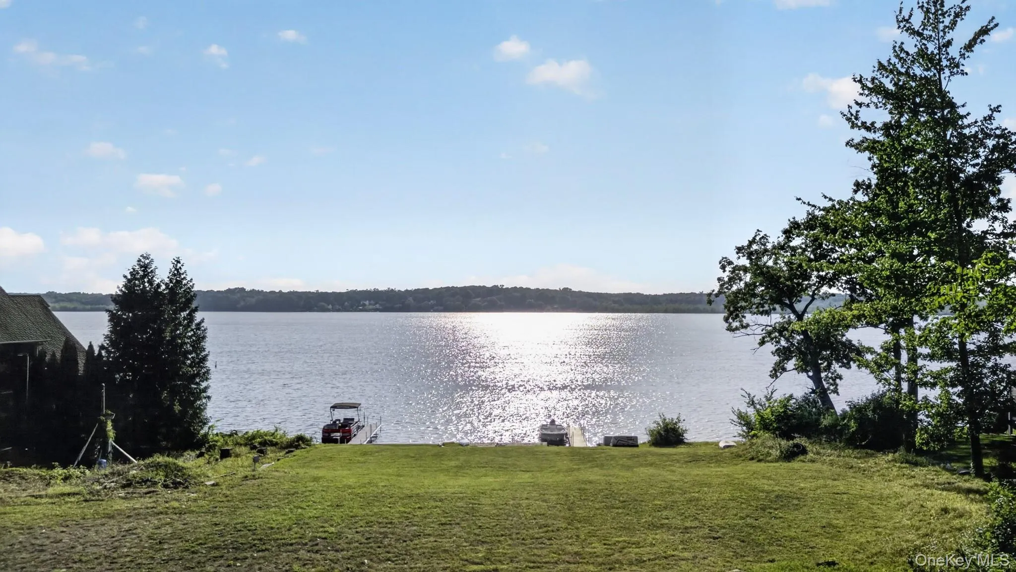 Expansive waterfront property featuring a wide lake frontage, a manicured lawn, established trees, and a private dock with a boat Expansive waterfront property featuring a wide lake frontage, a manicured lawn, established trees, and a private dock with a boat