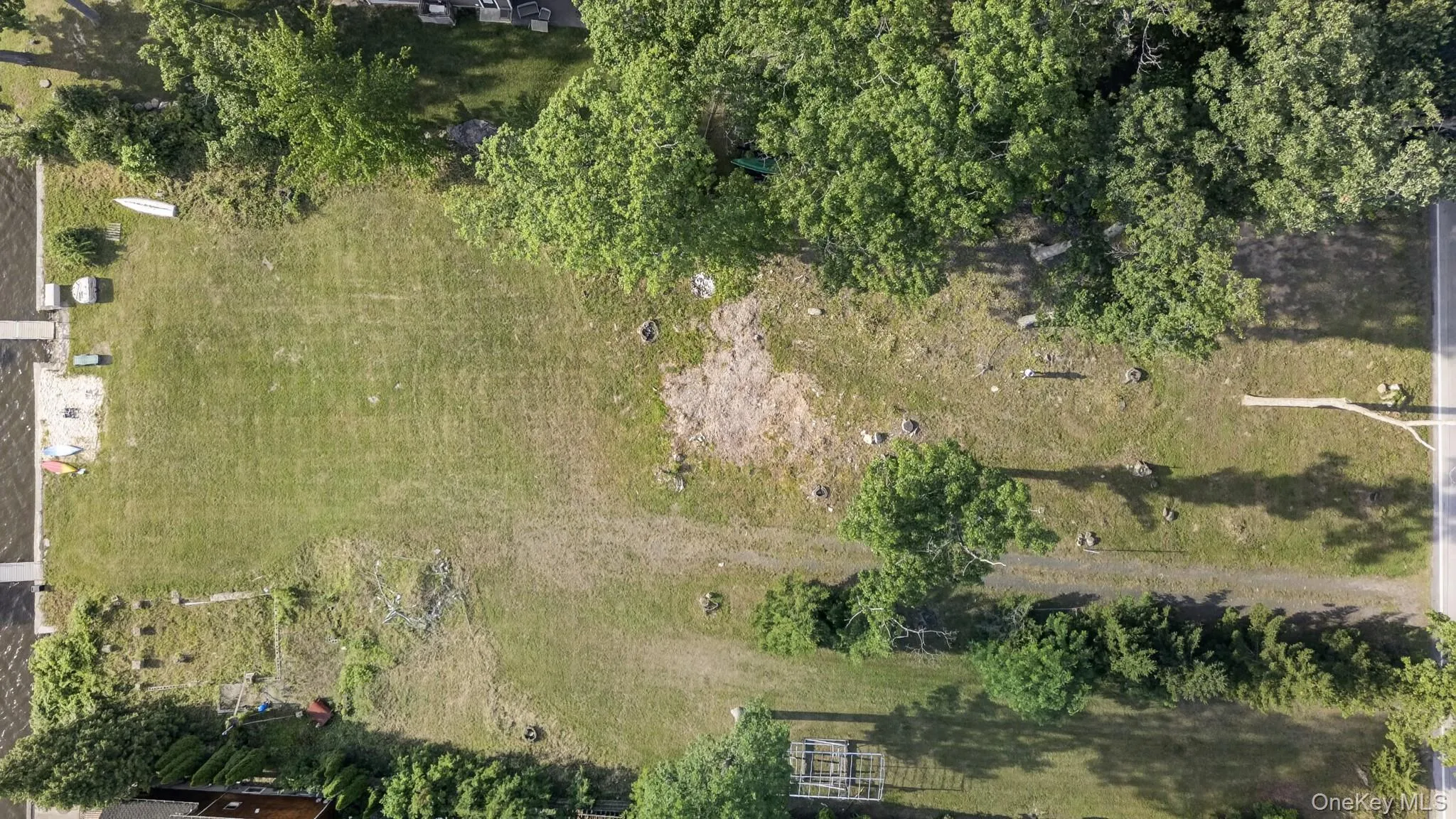 Expansive undeveloped lot featuring a grassed area, mature trees, and a paved road bordering the property Expansive undeveloped lot featuring a grassed area, mature trees, and a paved road bordering the property