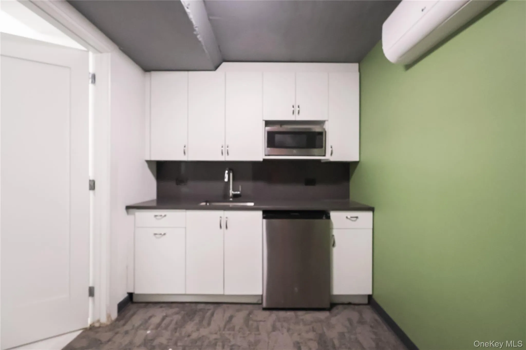 Kitchenette featuring white cabinetry, dark countertops, a stainless steel sink with a modern faucet, an integrated microwave, and a stainless steel dishwasher Kitchenette featuring white cabinetry, dark countertops, a stainless steel sink with a modern faucet, an integrated microwave, and a stainless steel dishwasher