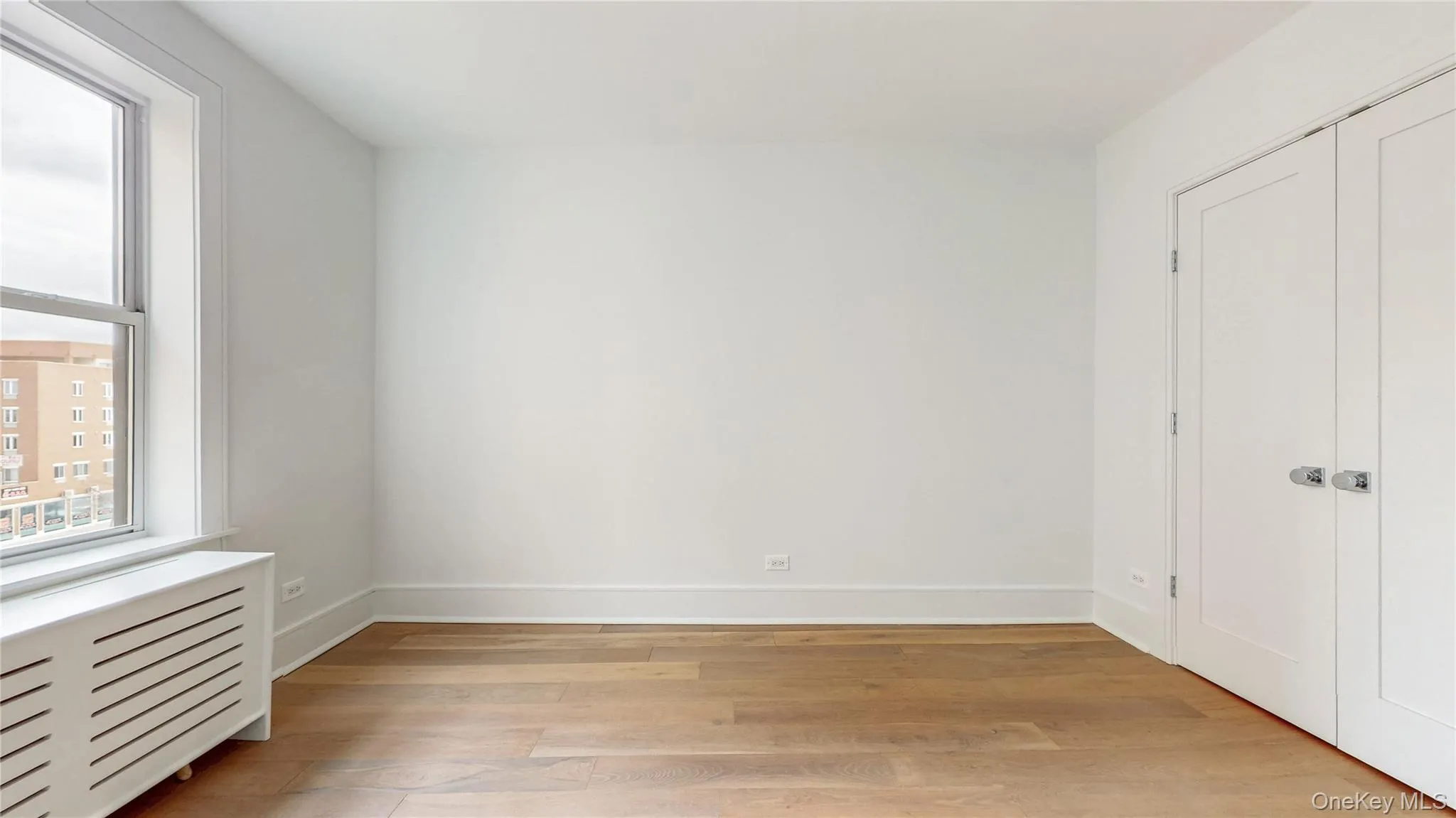 Bright interior space featuring wood-finish flooring, white walls, and a large window Bright interior space featuring wood-finish flooring, white walls, and a large window