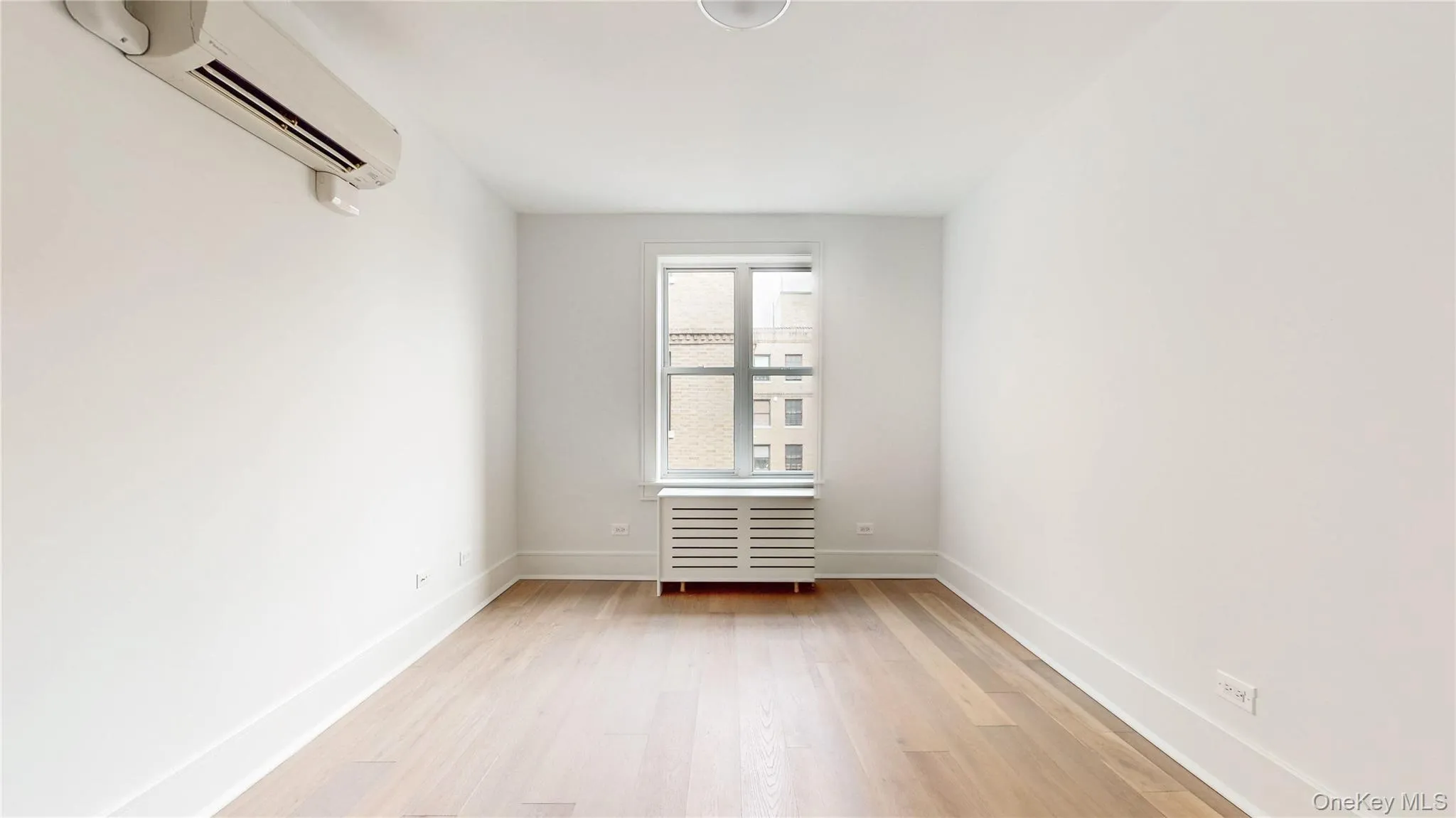 Bright room featuring wood-finish flooring, white baseboards, and a window with a radiator cover Bright room featuring wood-finish flooring, white baseboards, and a window with a radiator cover