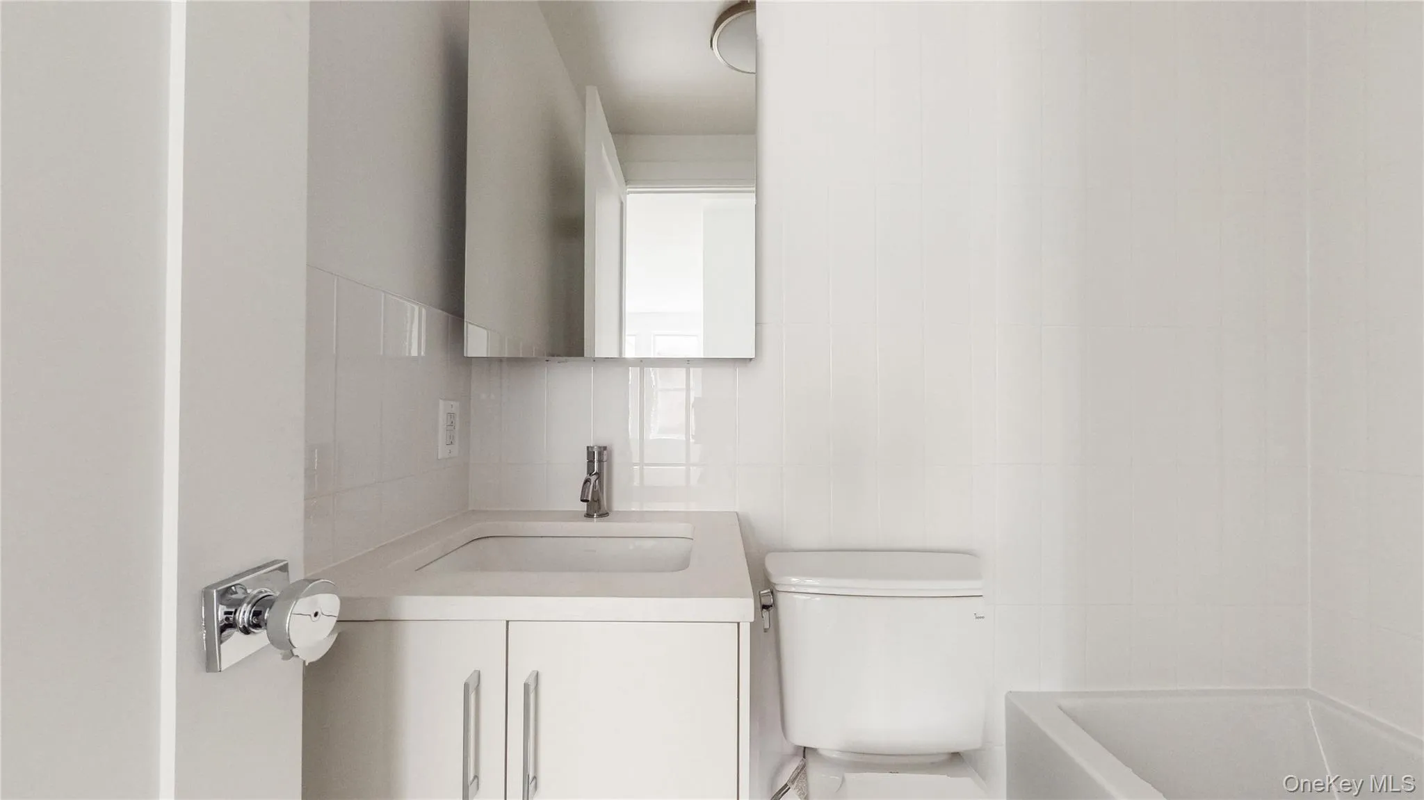 Compact bathroom featuring a white vanity with integrated sink, chrome faucet, and mirrored medicine cabinet Compact bathroom featuring a white vanity with integrated sink, chrome faucet, and mirrored medicine cabinet