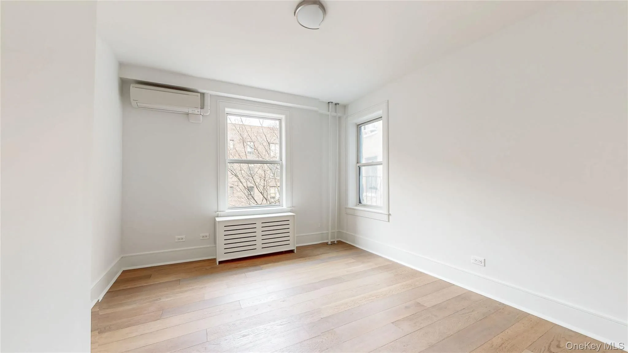Bright interior space featuring wood-finish flooring, white baseboards, and two windows Bright interior space featuring wood-finish flooring, white baseboards, and two windows