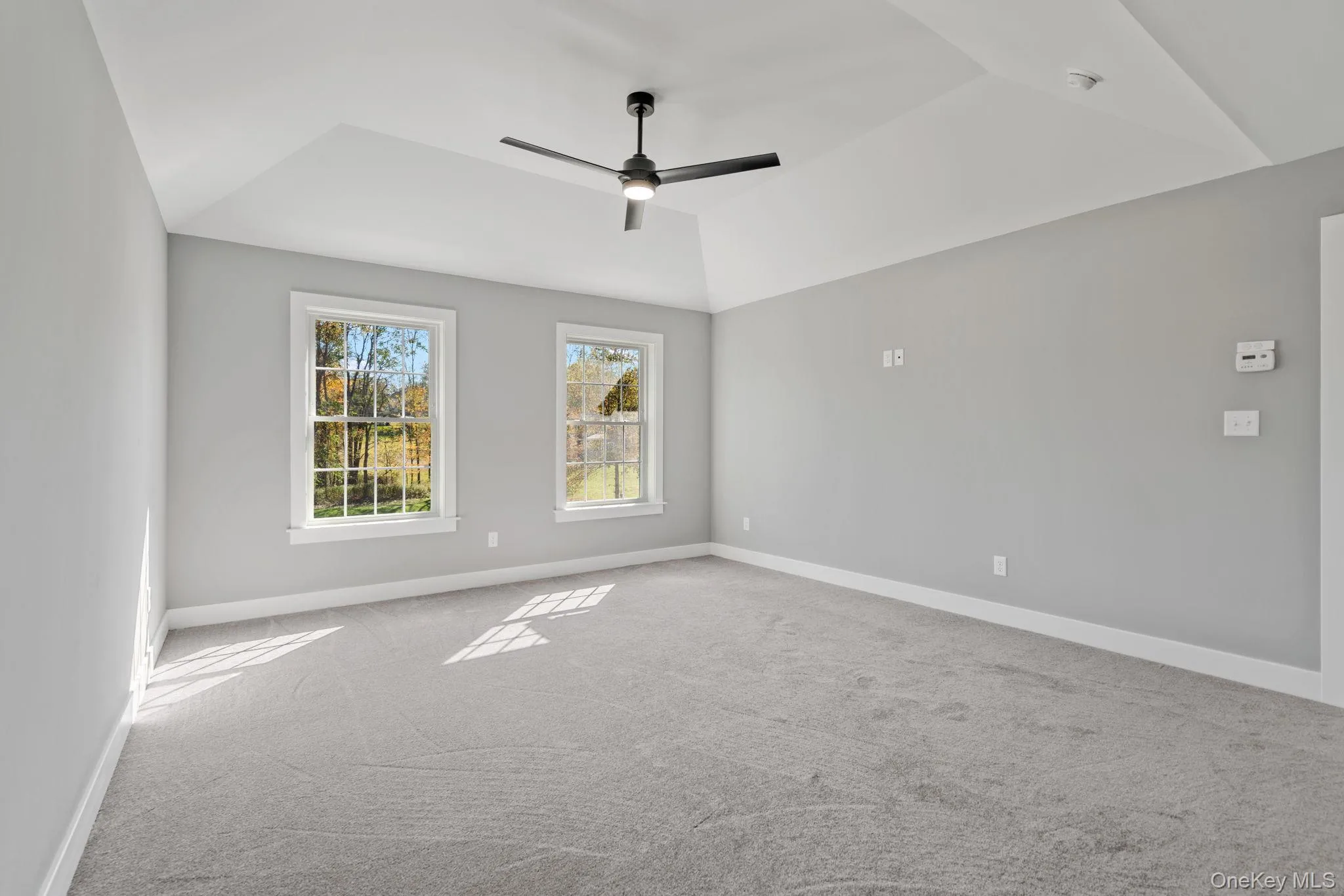Carpeted empty room featuring vaulted ceiling, baseboards, and a ceiling fan Carpeted empty room featuring vaulted ceiling, baseboards, and a ceiling fan