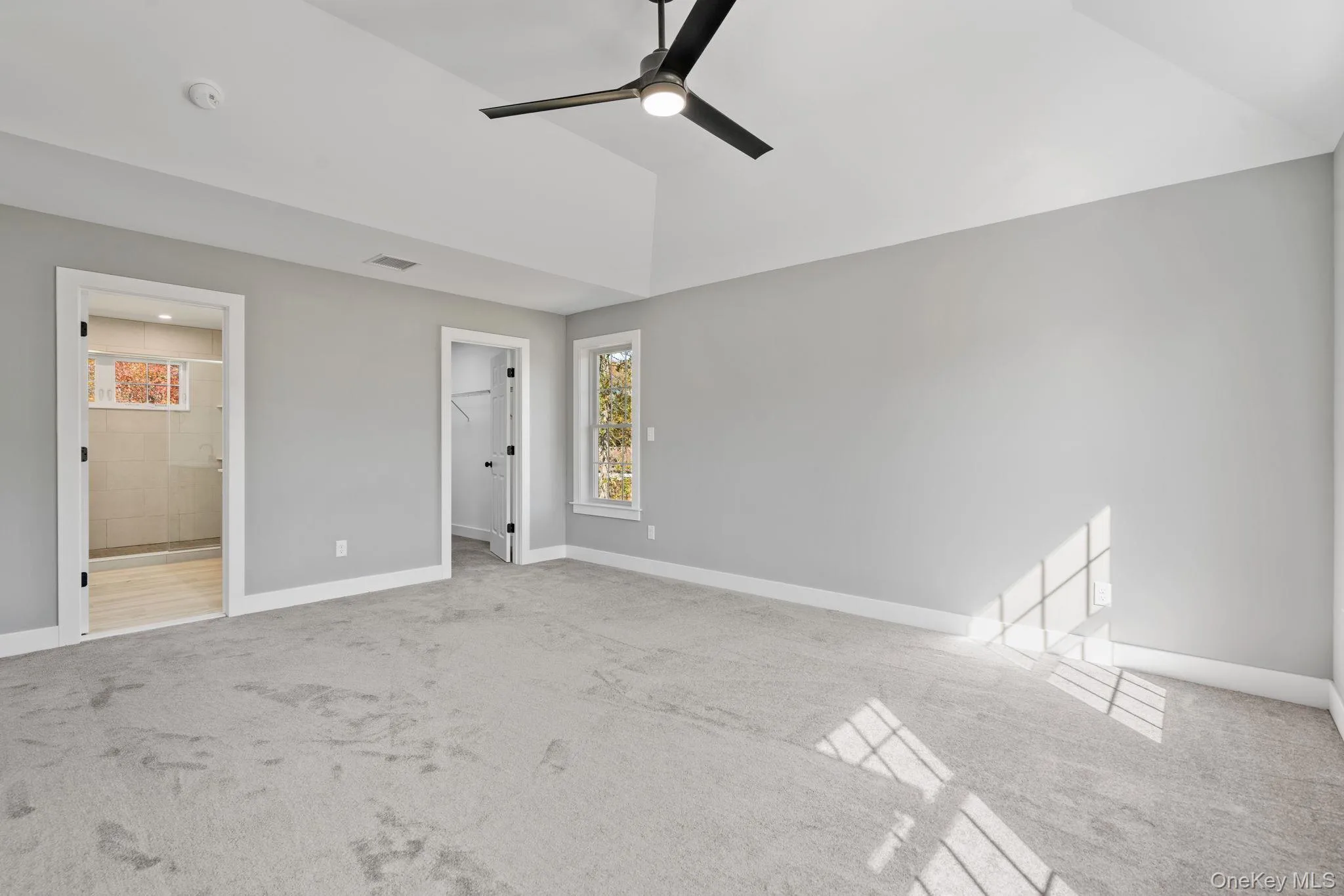 Unfurnished bedroom with baseboards, a walk in closet, carpet flooring, and vaulted ceiling Unfurnished bedroom with baseboards, a walk in closet, carpet flooring, and vaulted ceiling