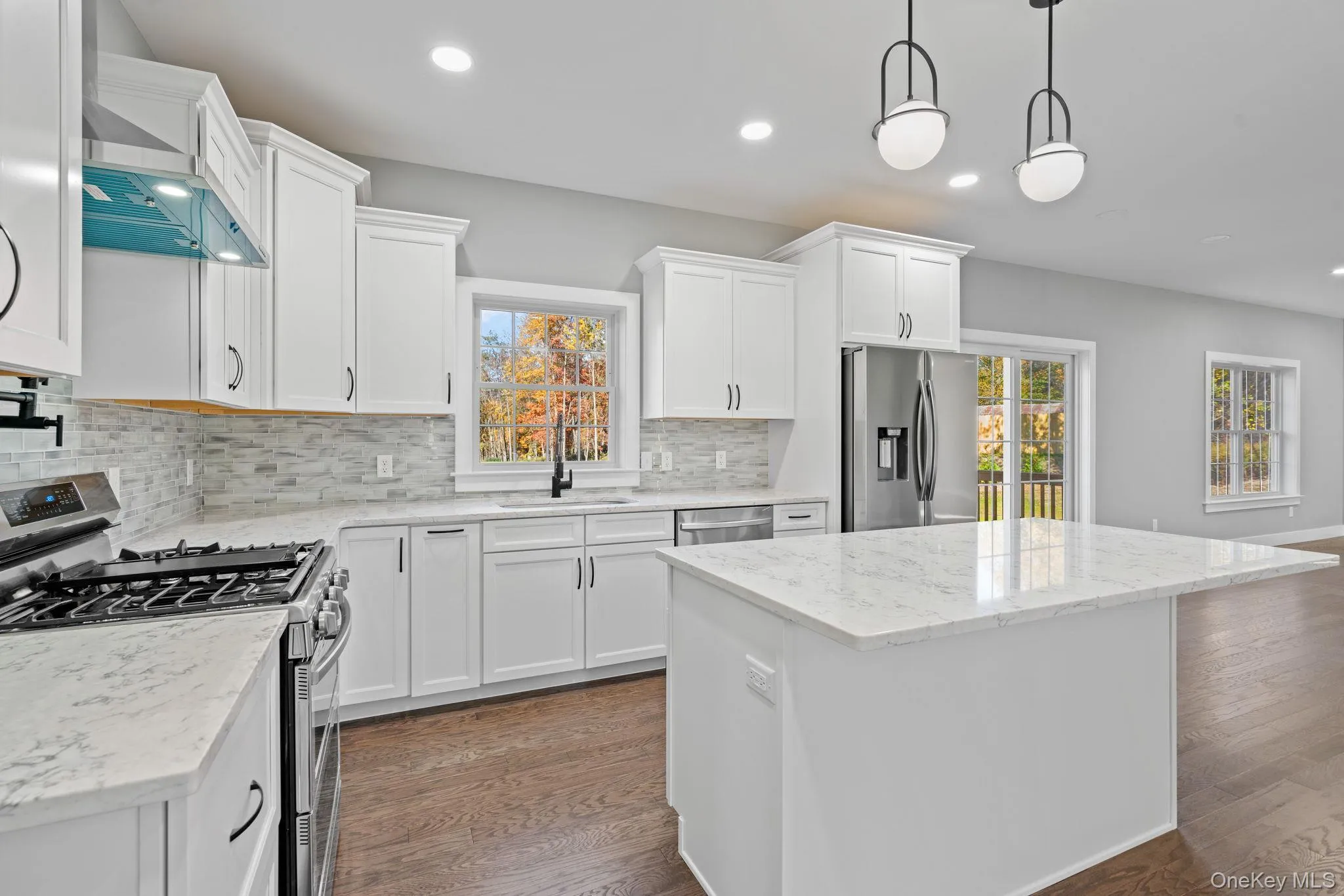 Kitchen featuring wall chimney range hood, white cabinetry, a kitchen island, a sink, and stainless steel appliances Kitchen featuring wall chimney range hood, white cabinetry, a kitchen island, a sink, and stainless steel appliances
