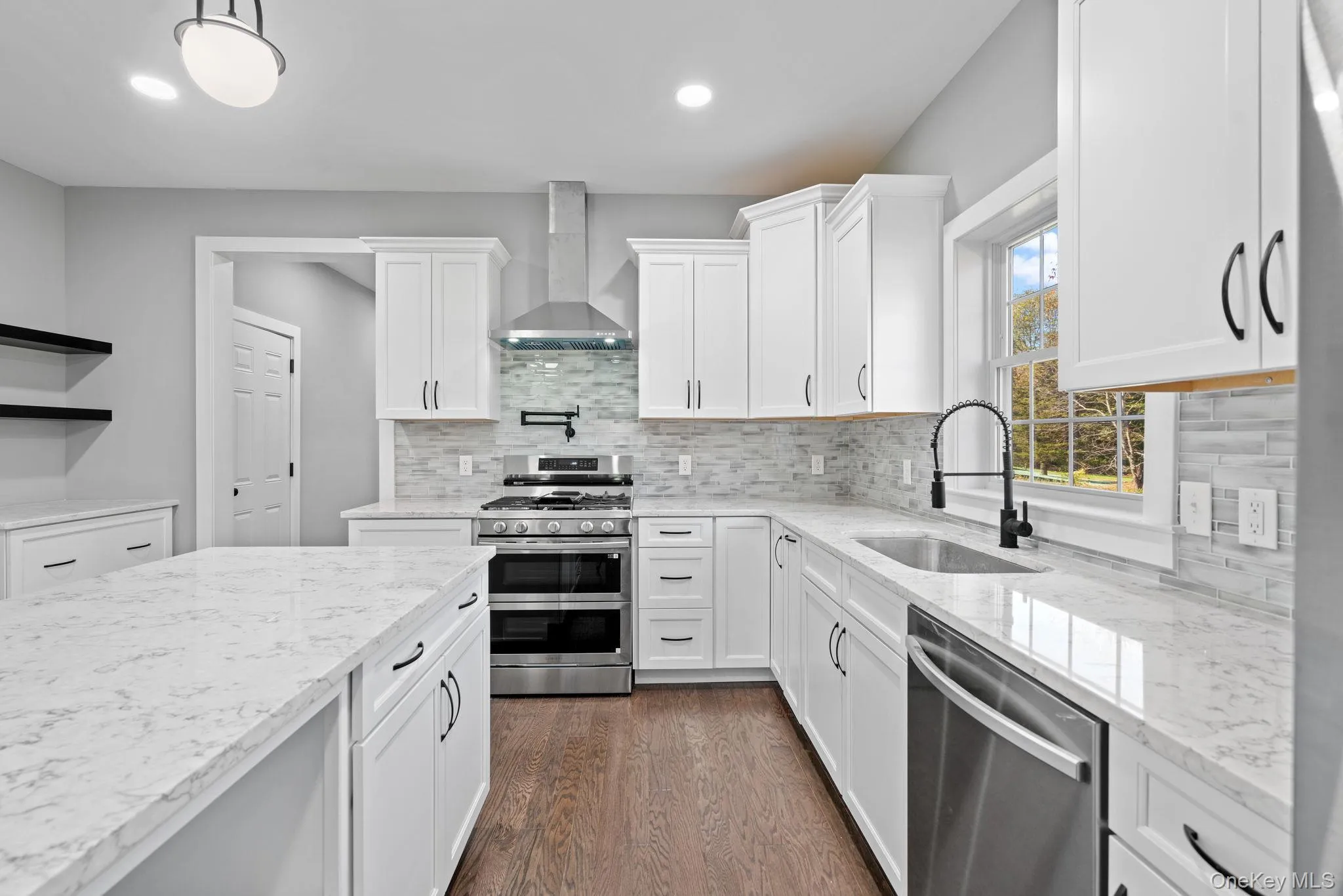 Kitchen featuring dark wood-type flooring, wall chimney range hood, white cabinetry, appliances with stainless steel finishes, and a sink Kitchen featuring dark wood-type flooring, wall chimney range hood, white cabinetry, appliances with stainless steel finishes, and a sink