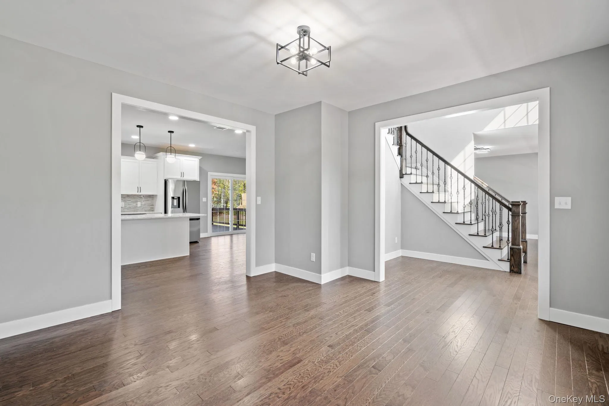 Unfurnished living room with a chandelier, dark wood-type flooring, stairway, and baseboards Unfurnished living room with a chandelier, dark wood-type flooring, stairway, and baseboards