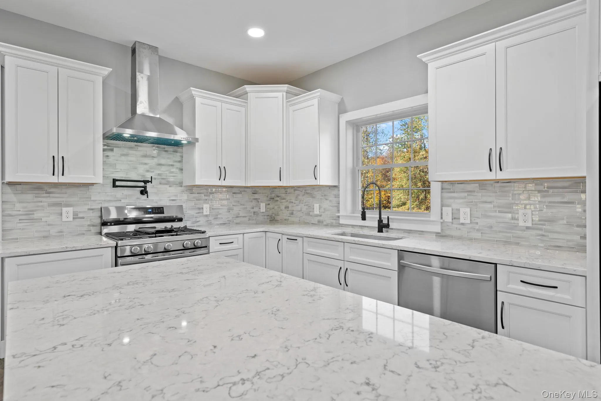 Kitchen featuring a sink, wall chimney range hood, white cabinetry, and stainless steel appliances Kitchen featuring a sink, wall chimney range hood, white cabinetry, and stainless steel appliances
