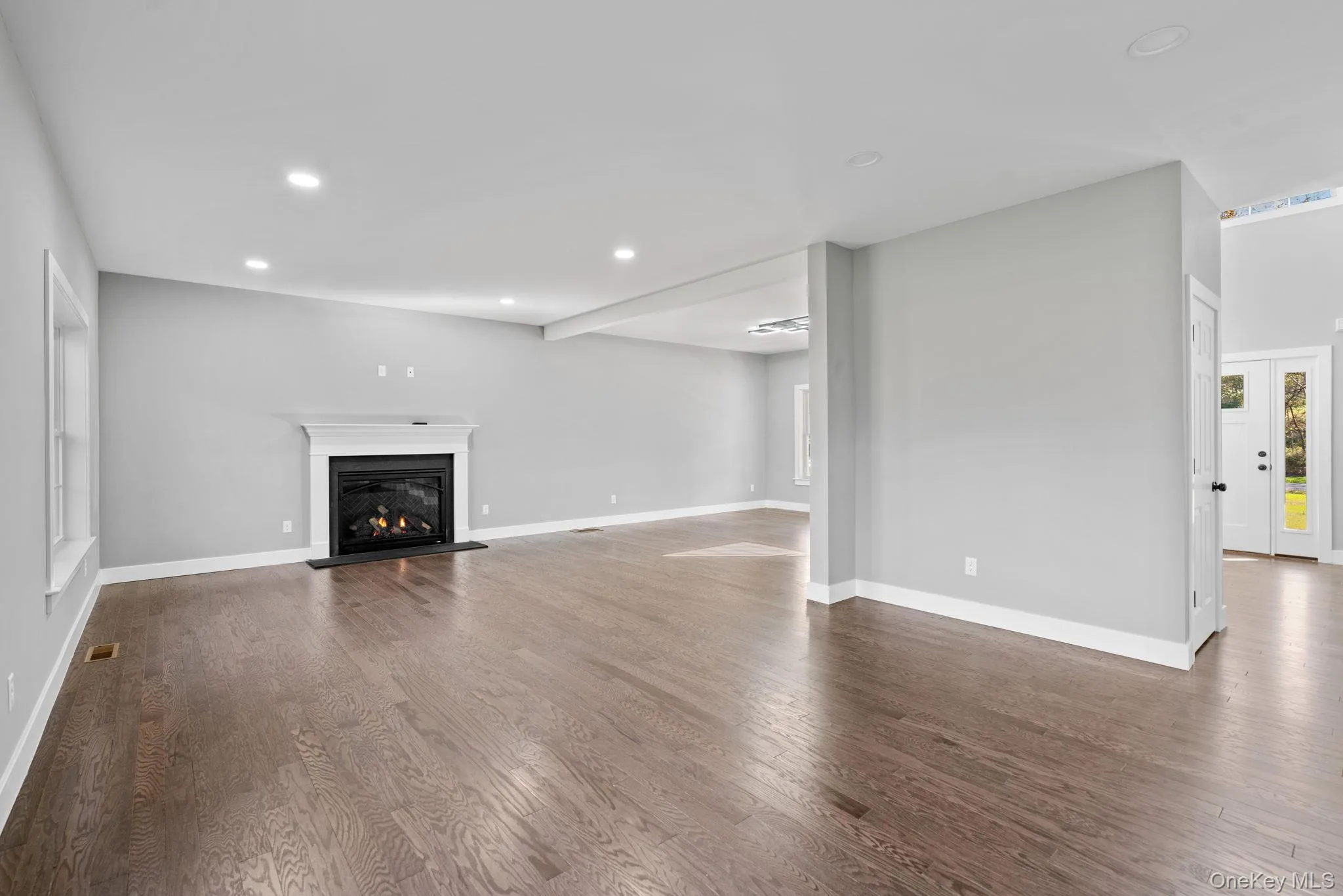 Unfurnished living room featuring a glass covered fireplace, baseboards, recessed lighting, dark wood-type flooring, and visible vents Unfurnished living room featuring a glass covered fireplace, baseboards, recessed lighting, dark wood-type flooring, and visible vents