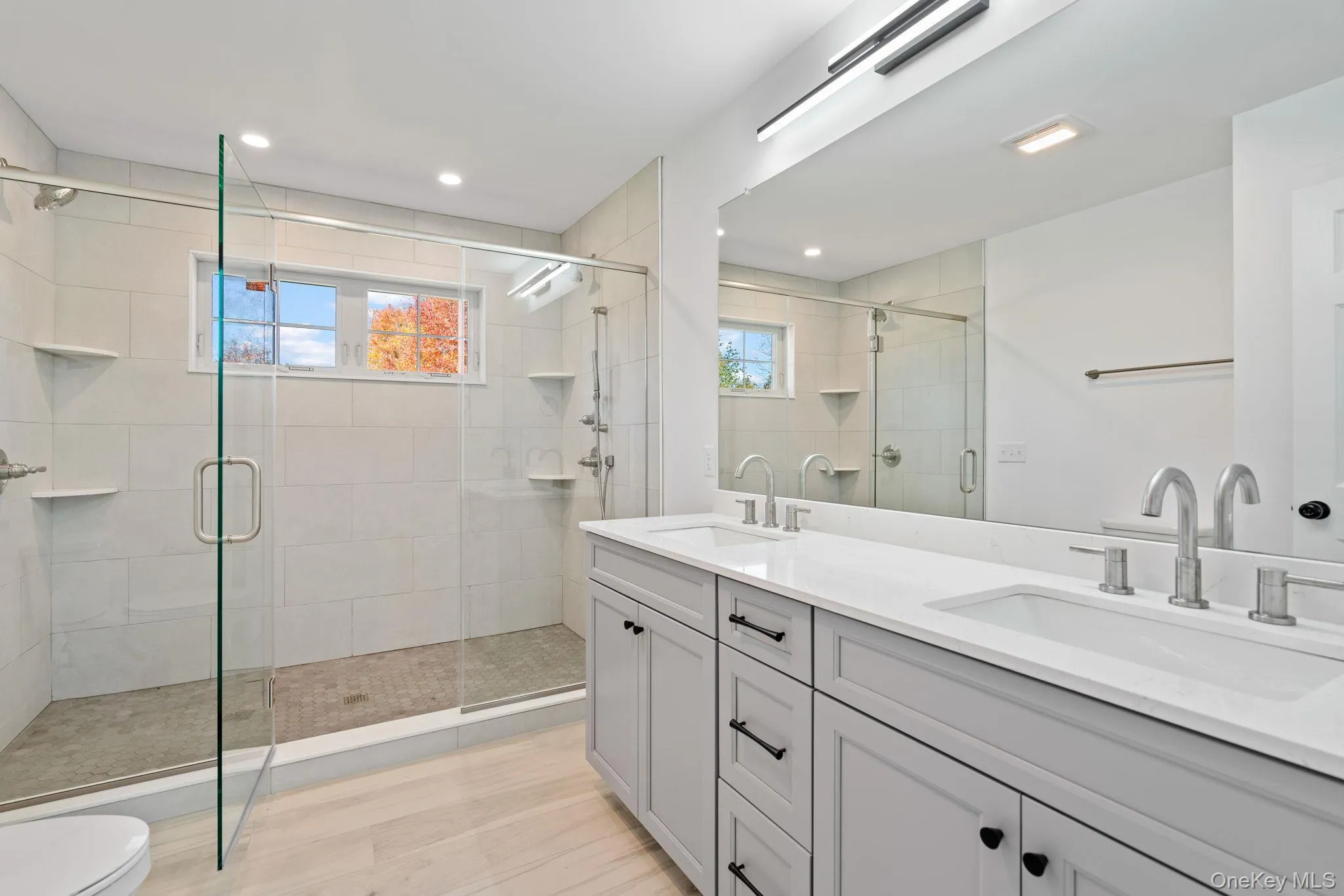 Bathroom featuring a sink, toilet, a shower stall, and double vanity Bathroom featuring a sink, toilet, a shower stall, and double vanity