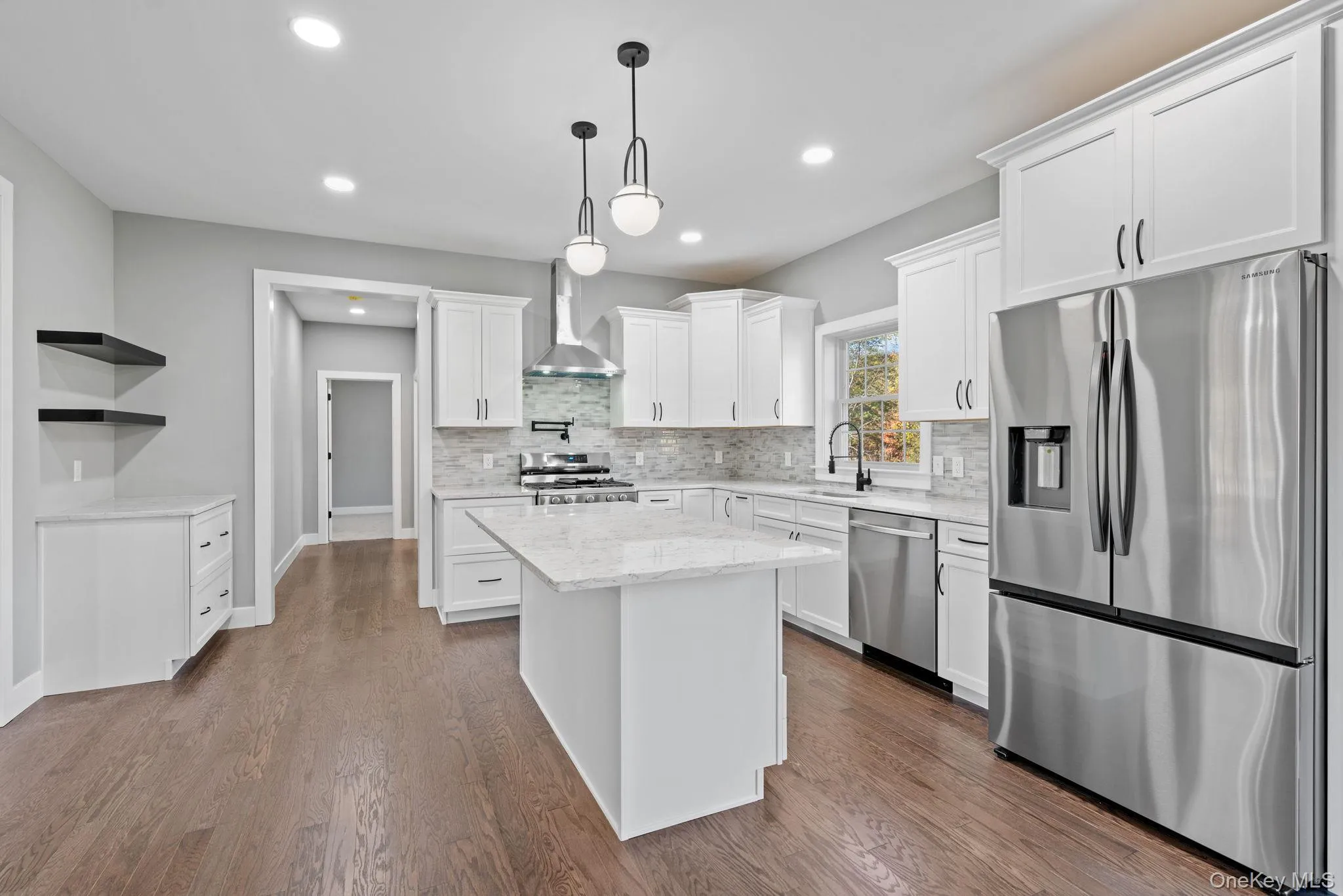 Kitchen featuring wall chimney range hood, a center island, appliances with stainless steel finishes, a sink, and backsplash Kitchen featuring wall chimney range hood, a center island, appliances with stainless steel finishes, a sink, and backsplash
