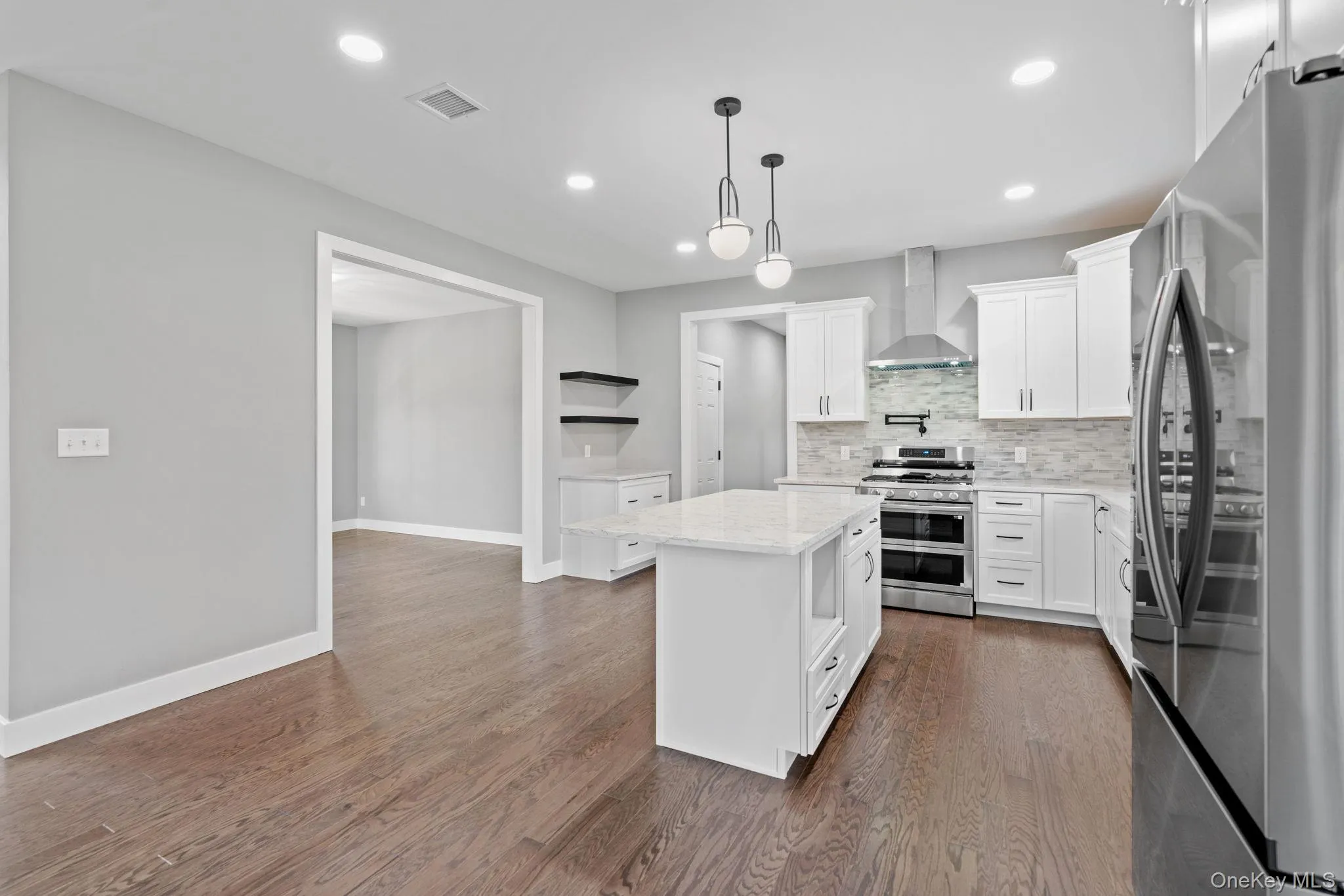 Kitchen featuring tasteful backsplash, visible vents, open shelves, wall chimney range hood, and stainless steel appliances Kitchen featuring tasteful backsplash, visible vents, open shelves, wall chimney range hood, and stainless steel appliances