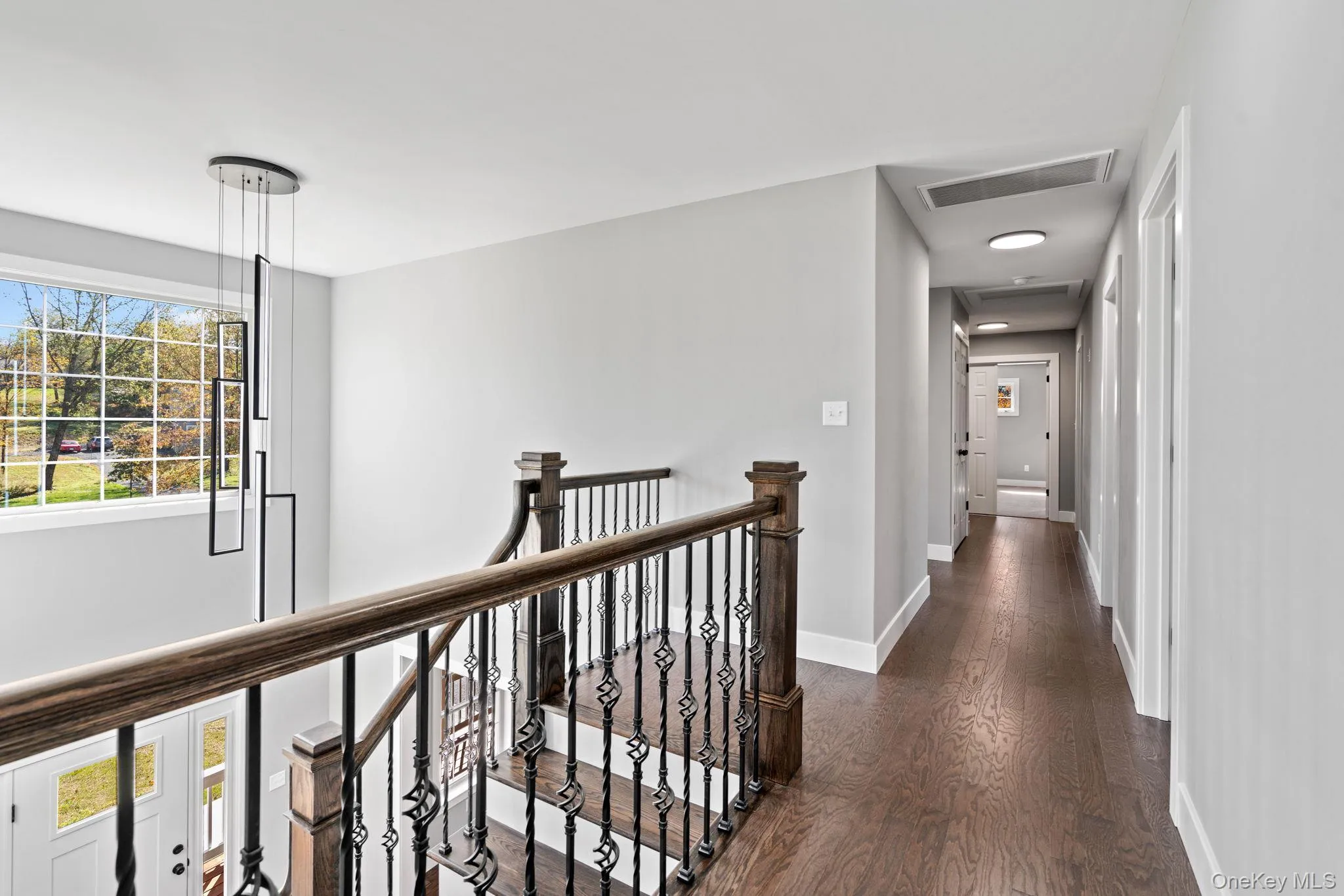 Hallway featuring dark wood-type flooring, an upstairs landing, baseboards, and visible vents Hallway featuring dark wood-type flooring, an upstairs landing, baseboards, and visible vents