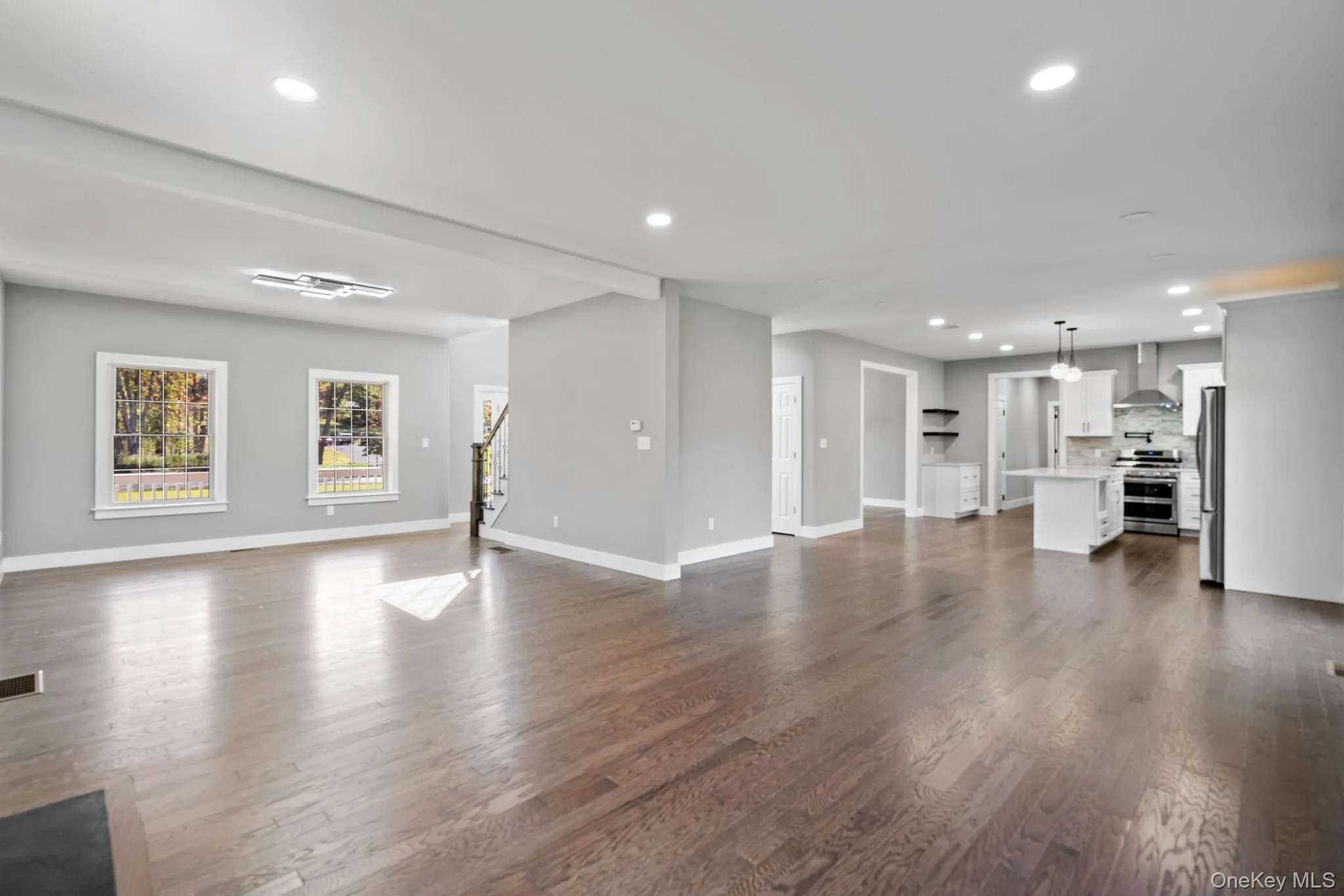 Unfurnished living room featuring recessed lighting, dark wood-style flooring, baseboards, and stairs Unfurnished living room featuring recessed lighting, dark wood-style flooring, baseboards, and stairs