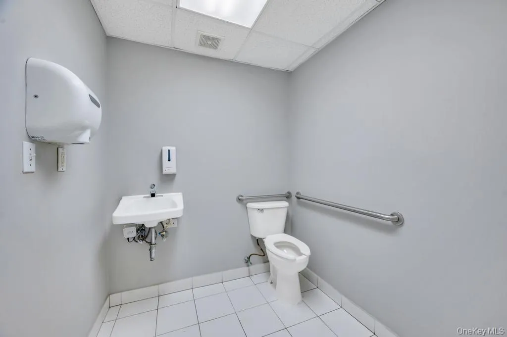 Commercial restroom featuring a wall-mounted sink, white toilet, and grab bars Commercial restroom featuring a wall-mounted sink, white toilet, and grab bars