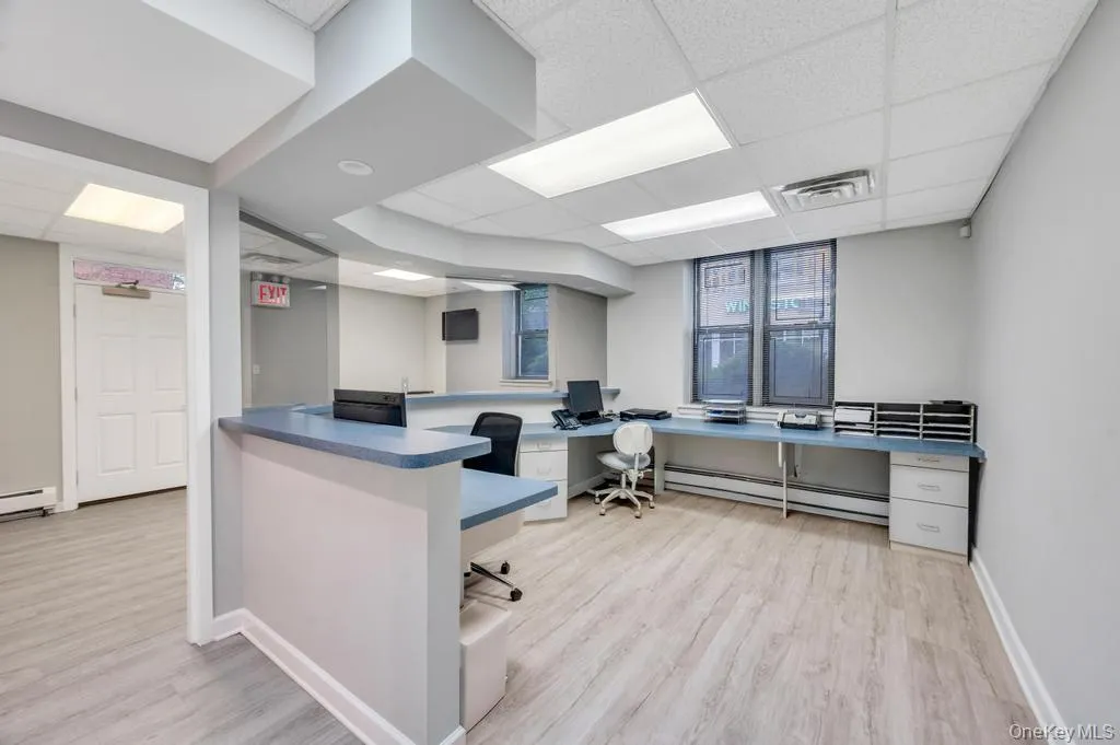 Reception area featuring wood-finish flooring, a suspended ceiling with recessed lighting, and a built-in curved counter with a blue countertop Reception area featuring wood-finish flooring, a suspended ceiling with recessed lighting, and a built-in curved counter with a blue countertop